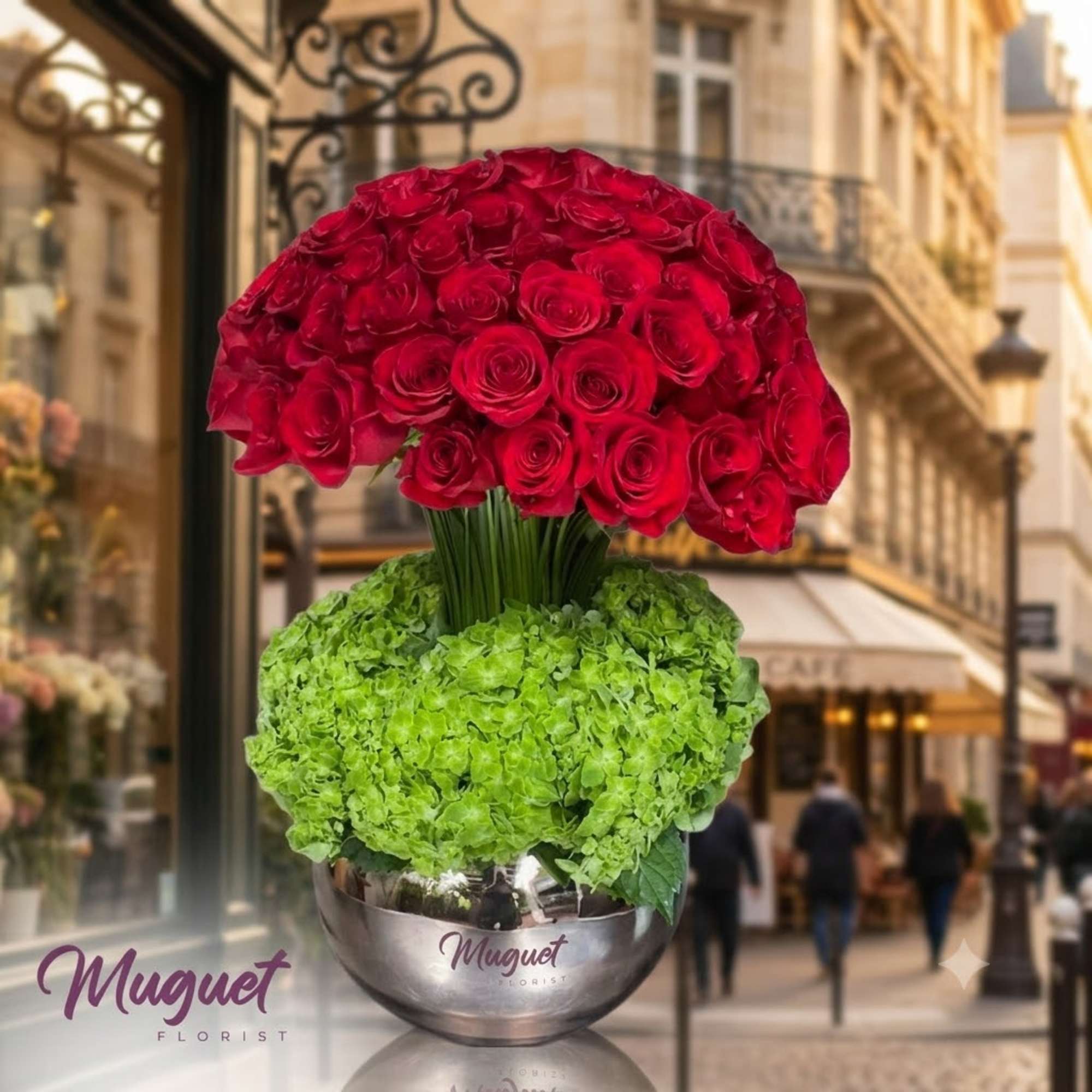 Red rose arrangement above a green hydrangea mound in a silver bowl