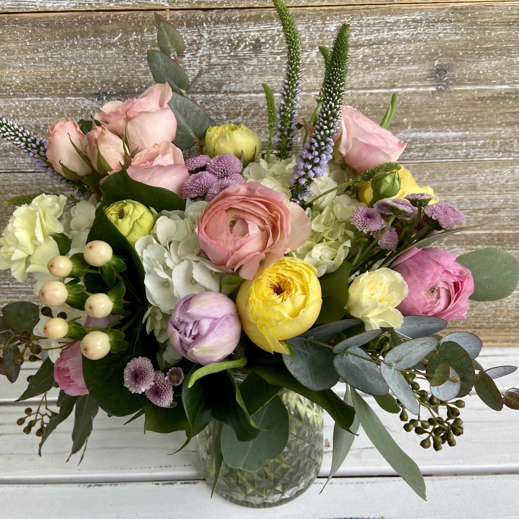 Pastel bouquet of roses, ranunculus, and hydrangeas in a clear glass vase