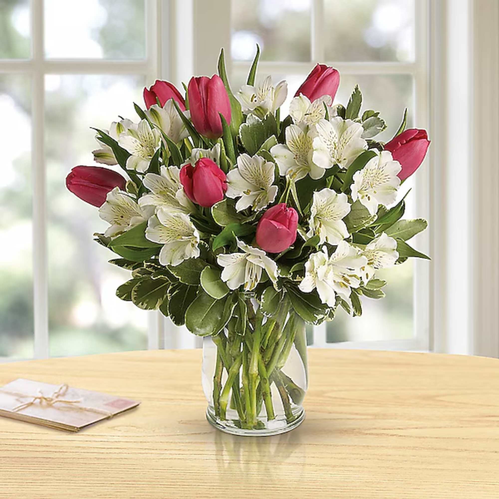 Pink tulips and white flowers in a clear glass vase