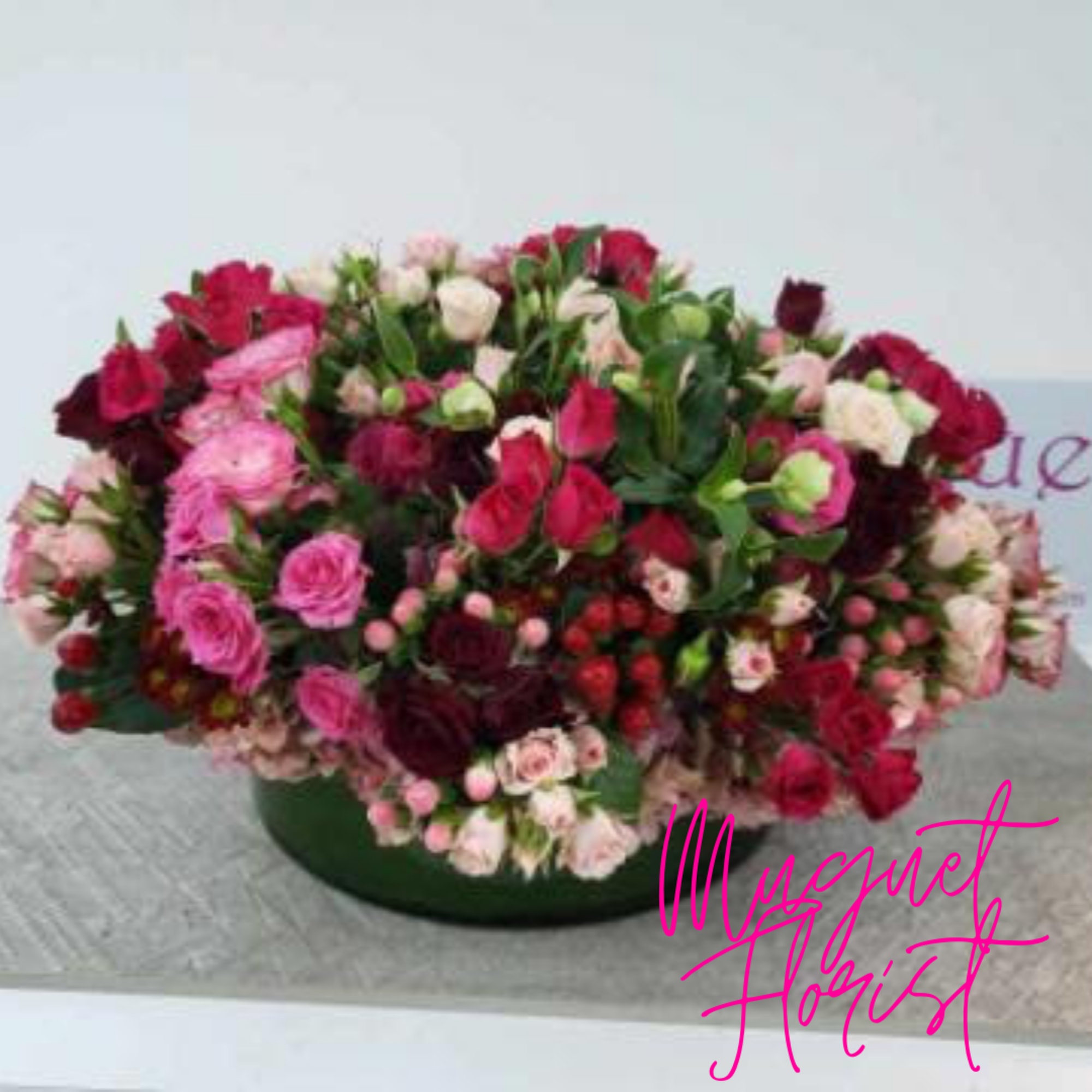 Large mixed bouquet of pink, red, and white flowers in a low green container