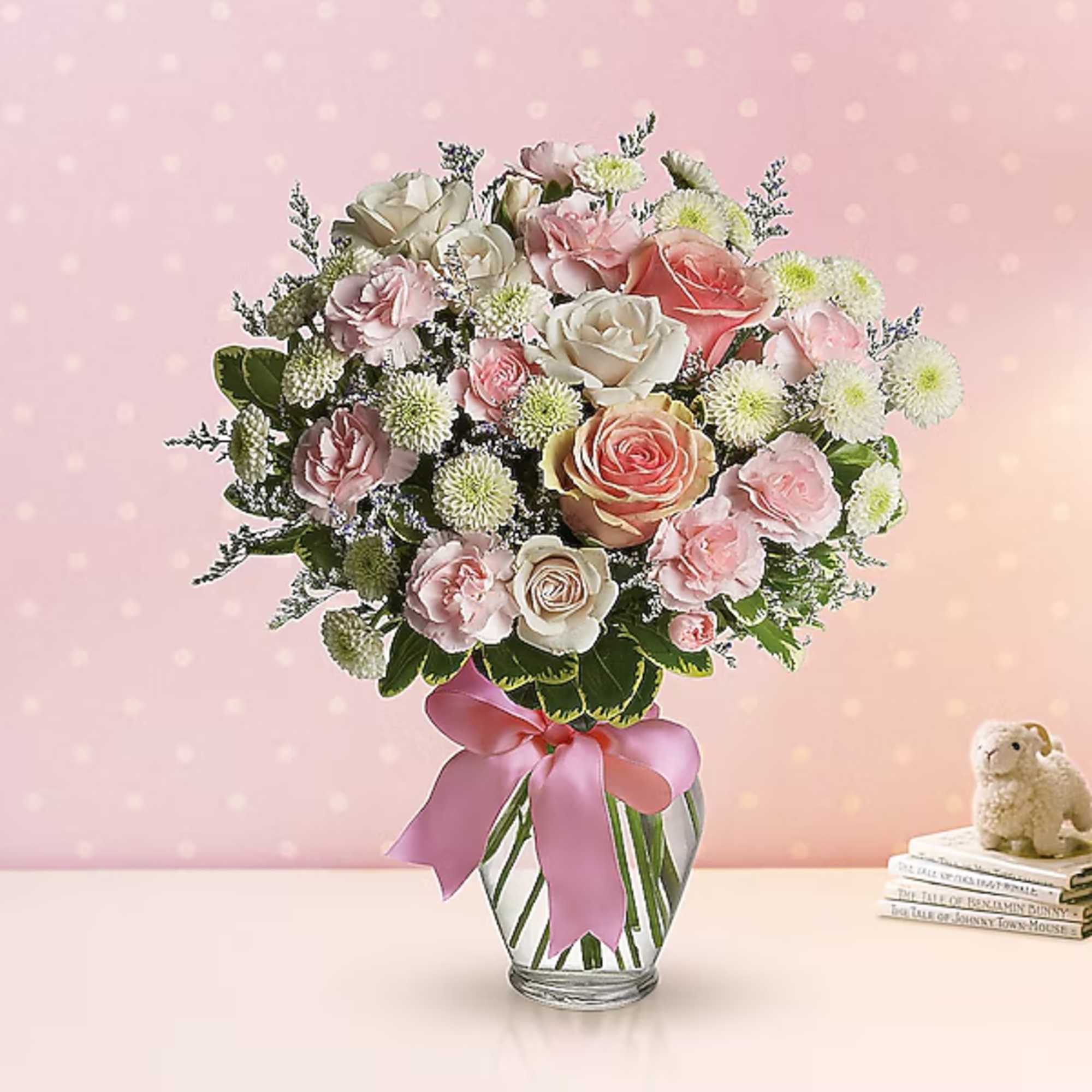 Pink and white rose bouquet in a clear glass vase with a pink ribbon