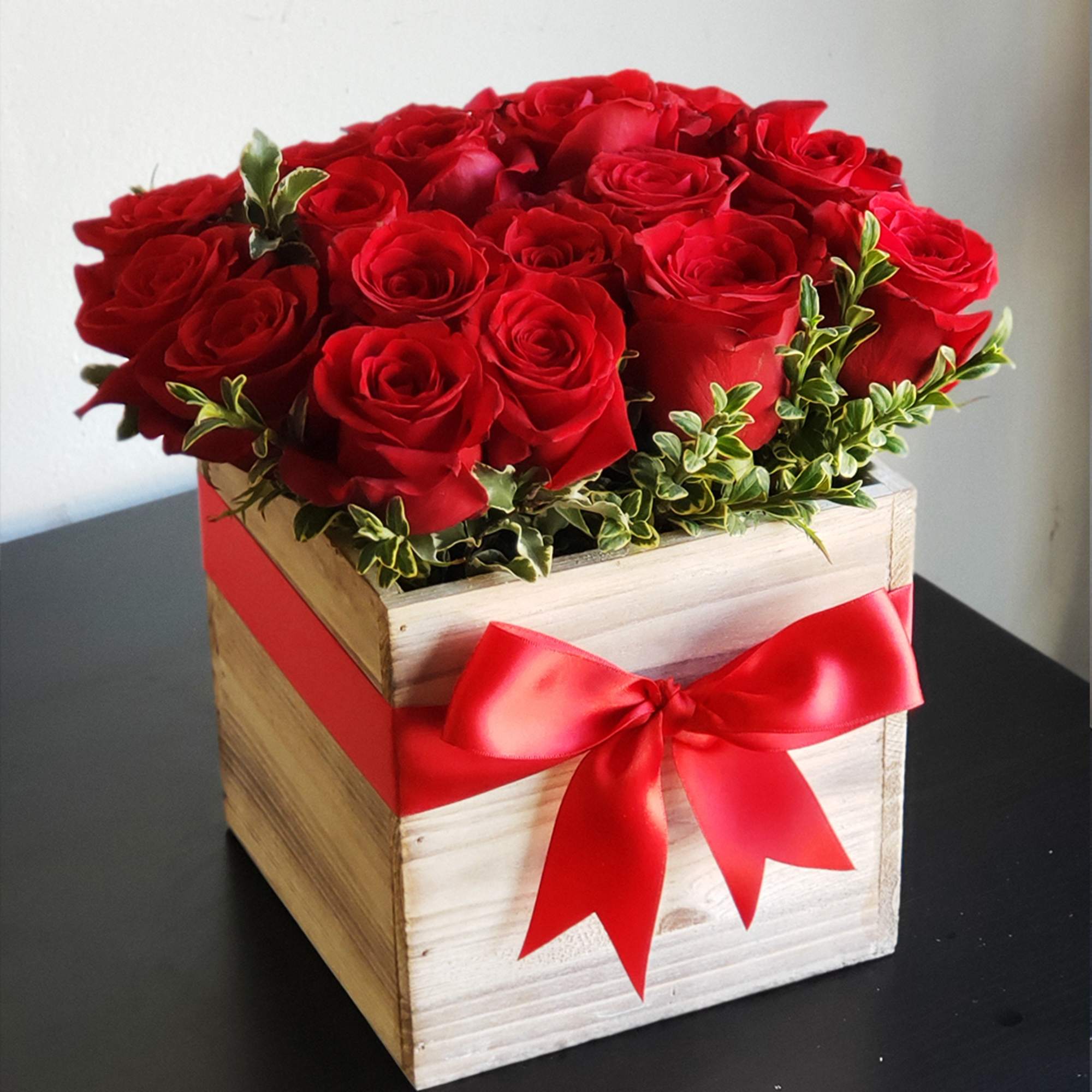 Red roses arranged in a wooden box with a red ribbon