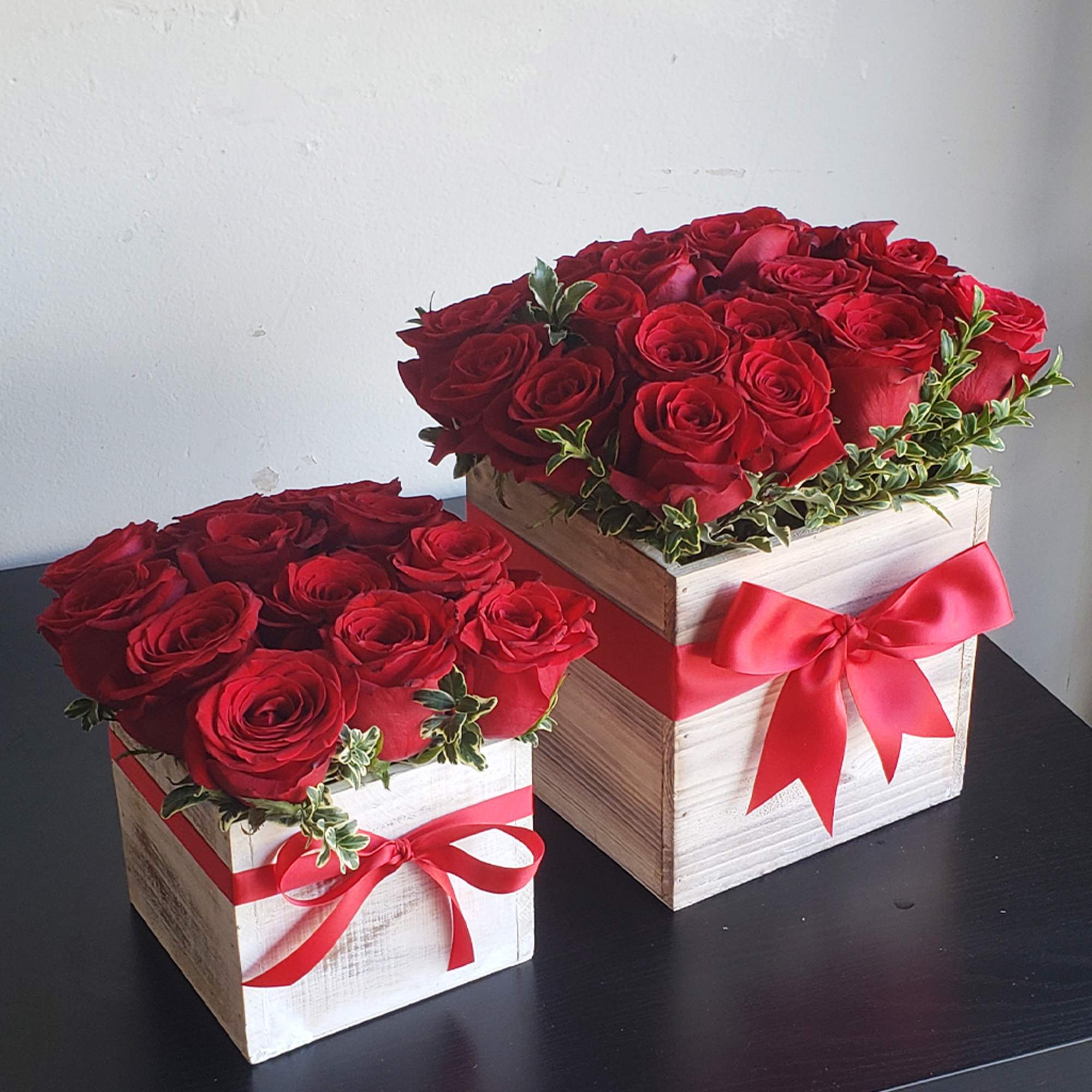 Two red rose arrangements in white wooden boxes with red ribbons