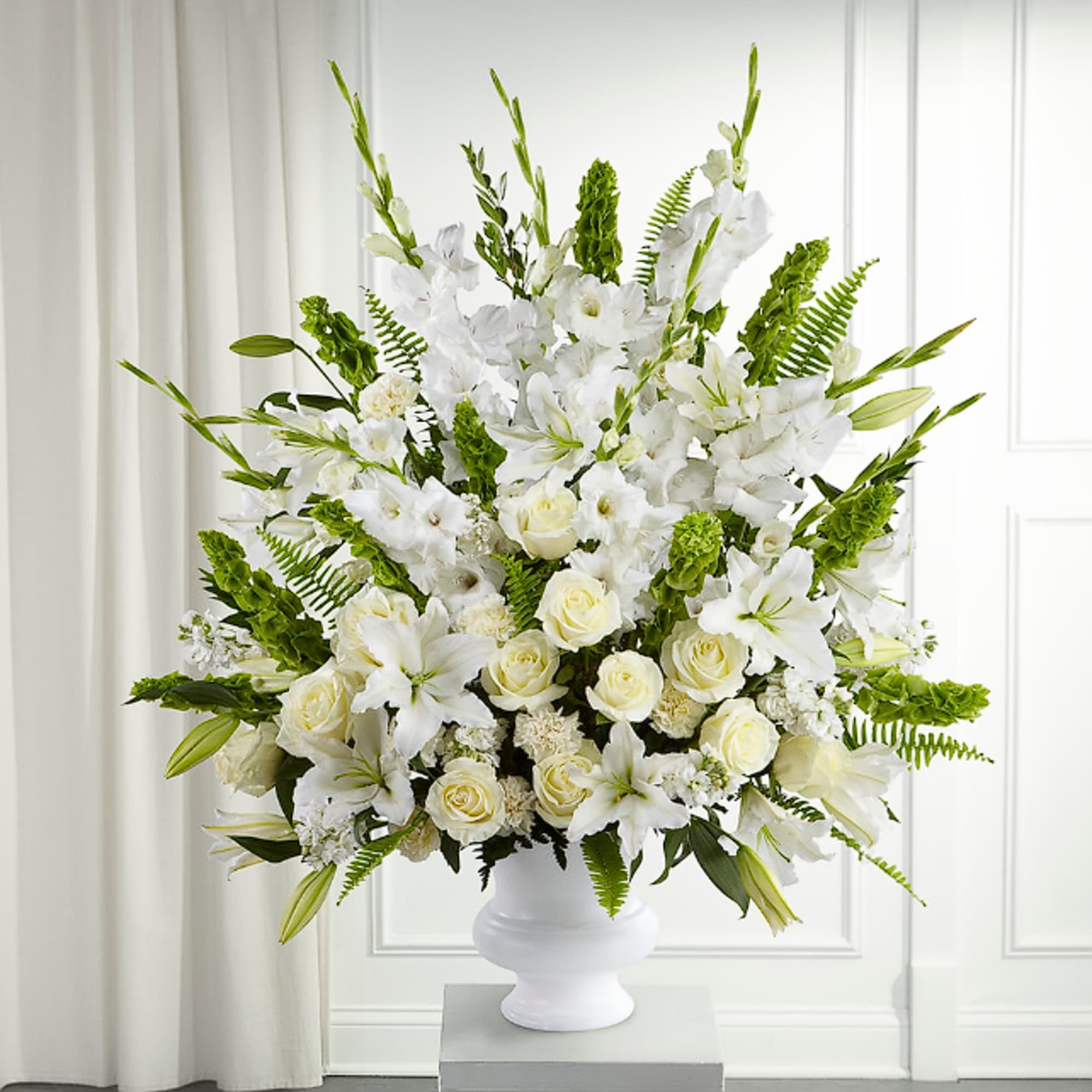 White lilies and roses arranged in a white pedestal vase