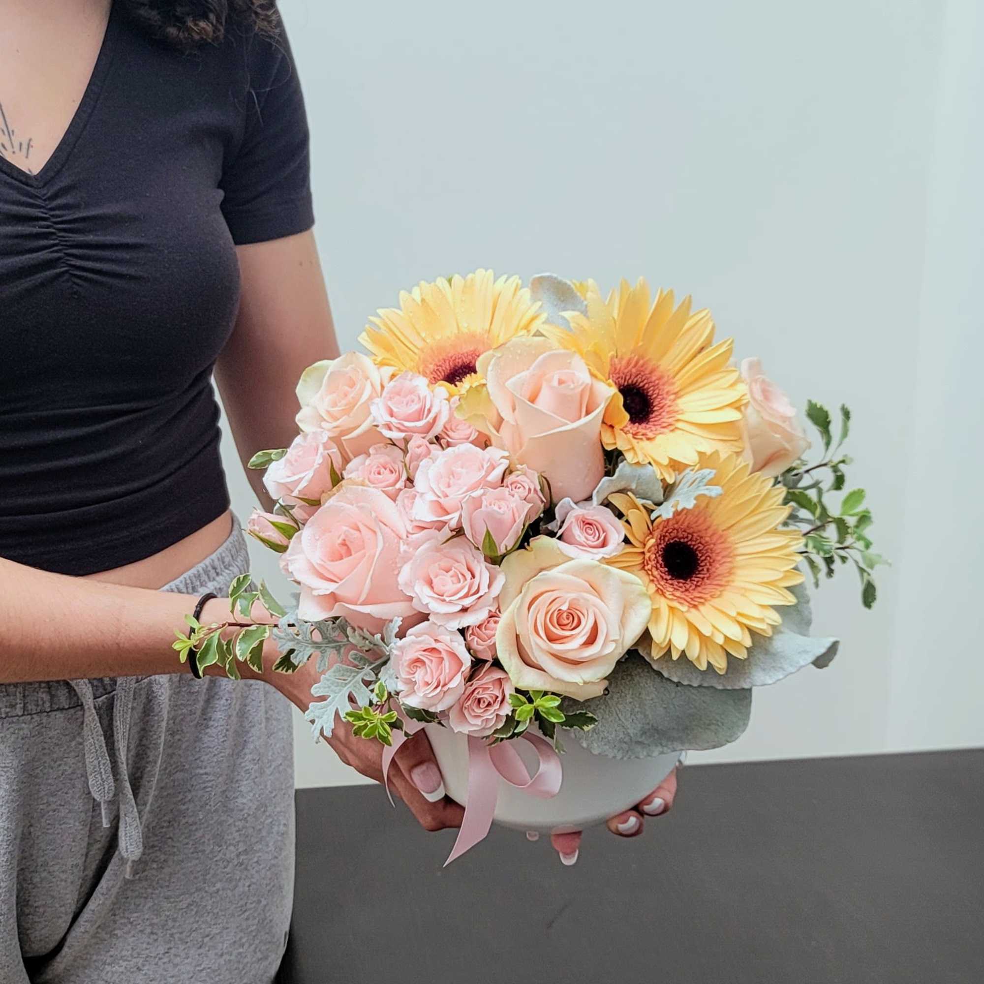 Handheld bouquet of pale pink roses and yellow gerbera daisies in a white bowl