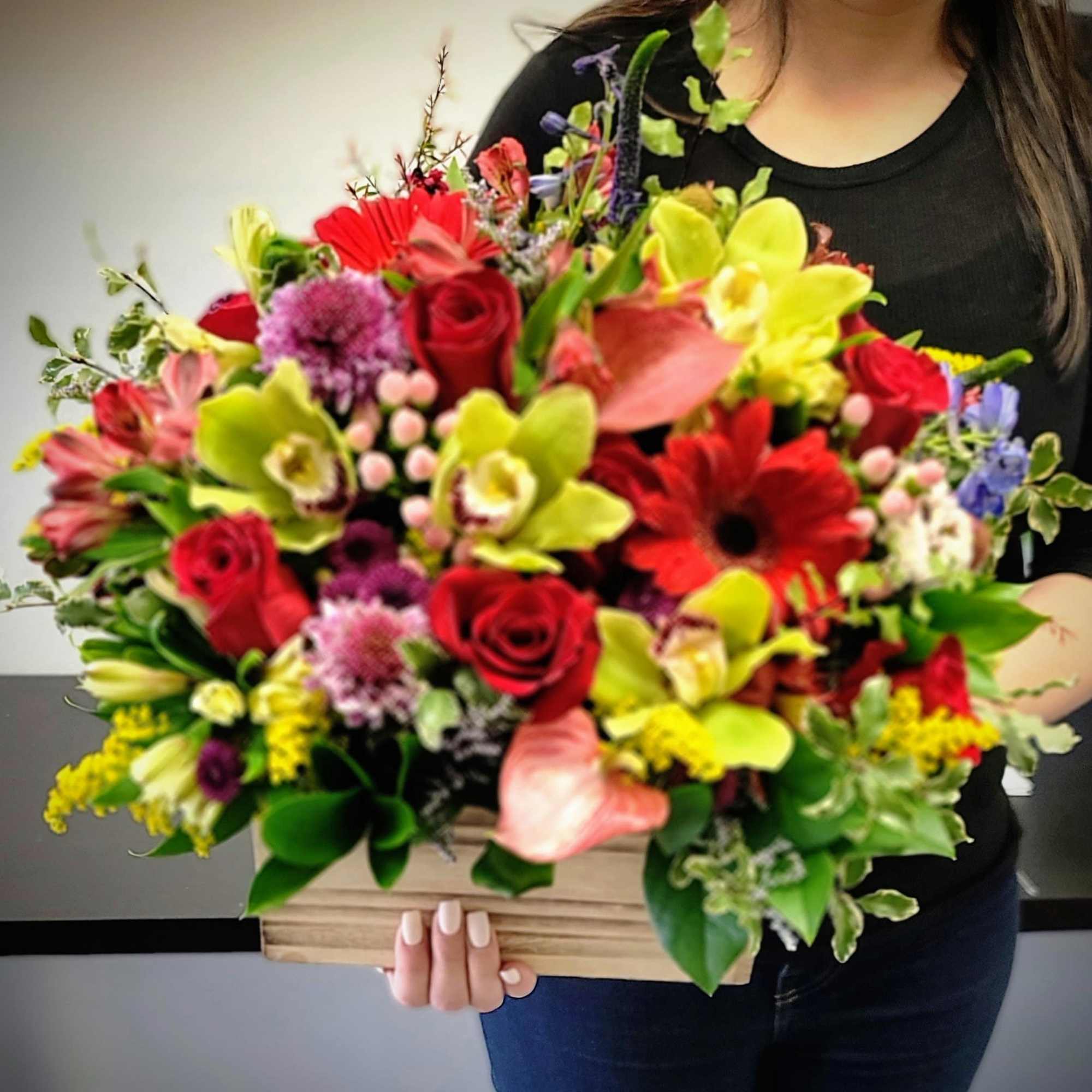 Mixed bouquet in a wooden box with red, yellow, and pink flowers