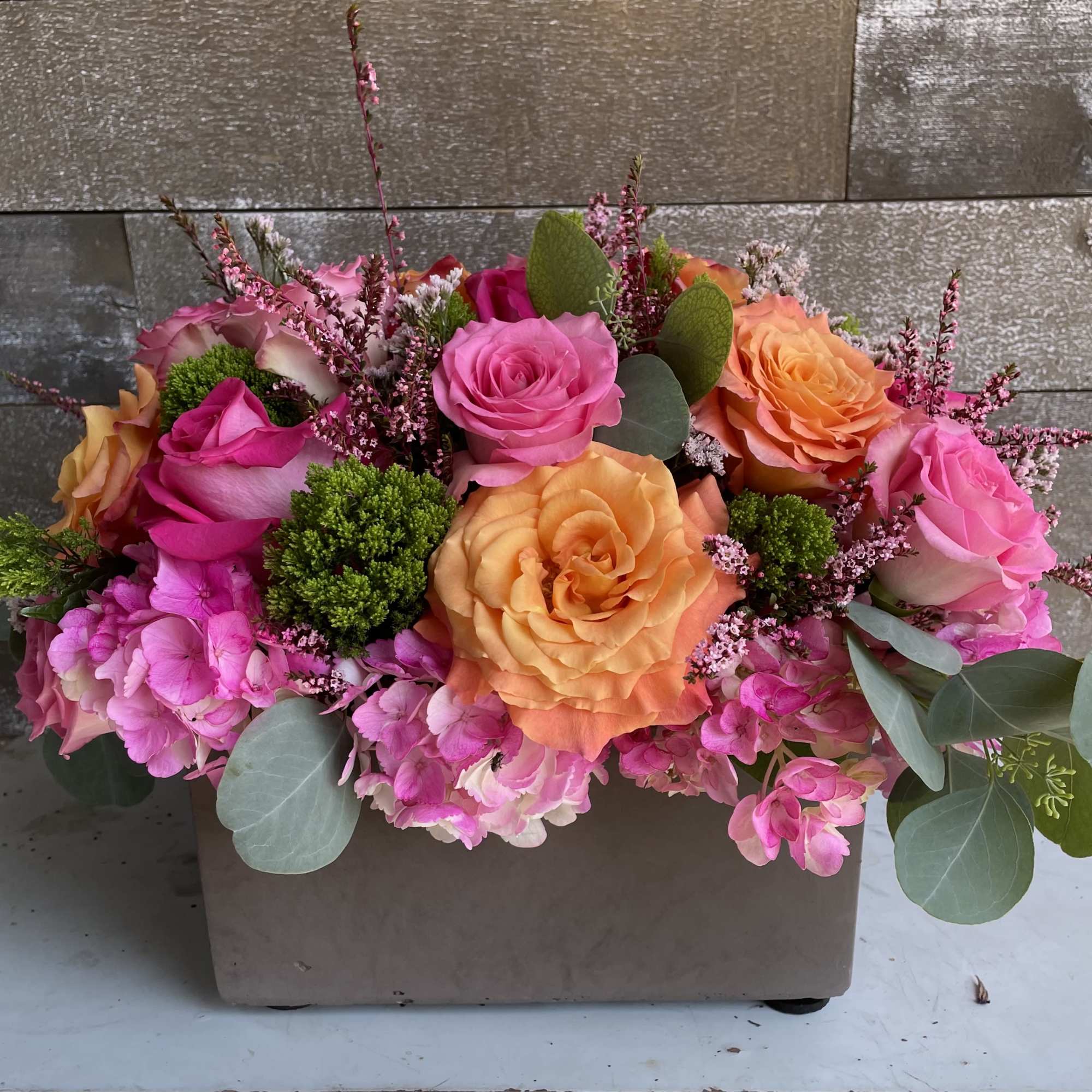 Pink and peach roses arranged in a rectangular box with greenery