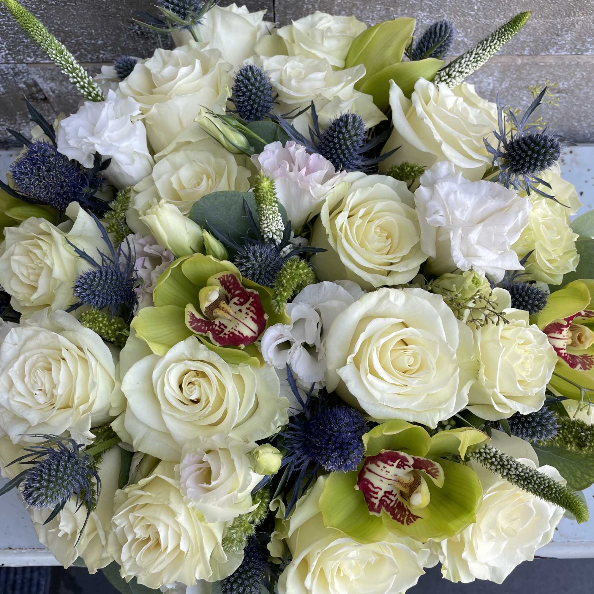 Bouquet of white roses with green orchids and blue thistle accents