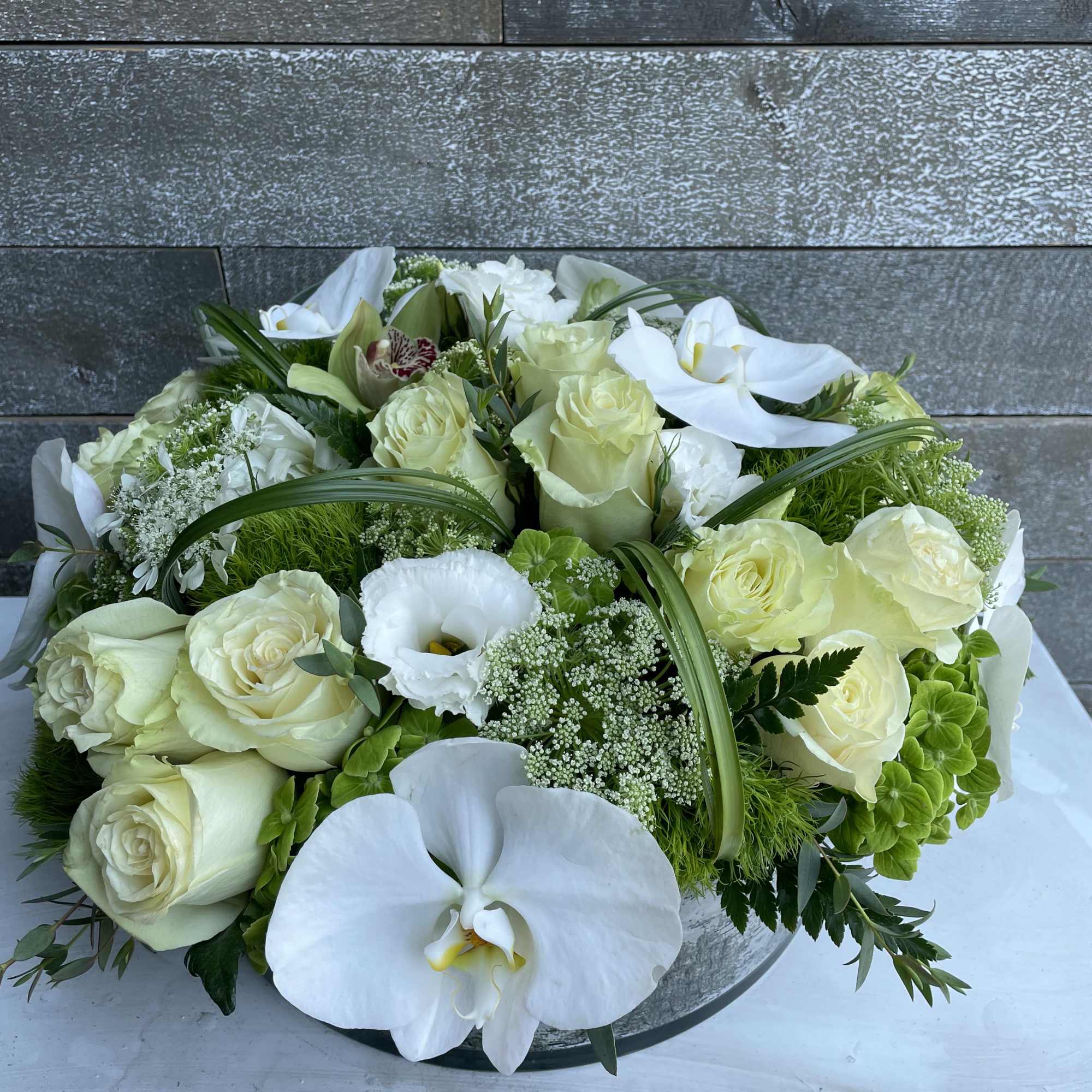 White roses and orchids arranged in a low round centerpiece