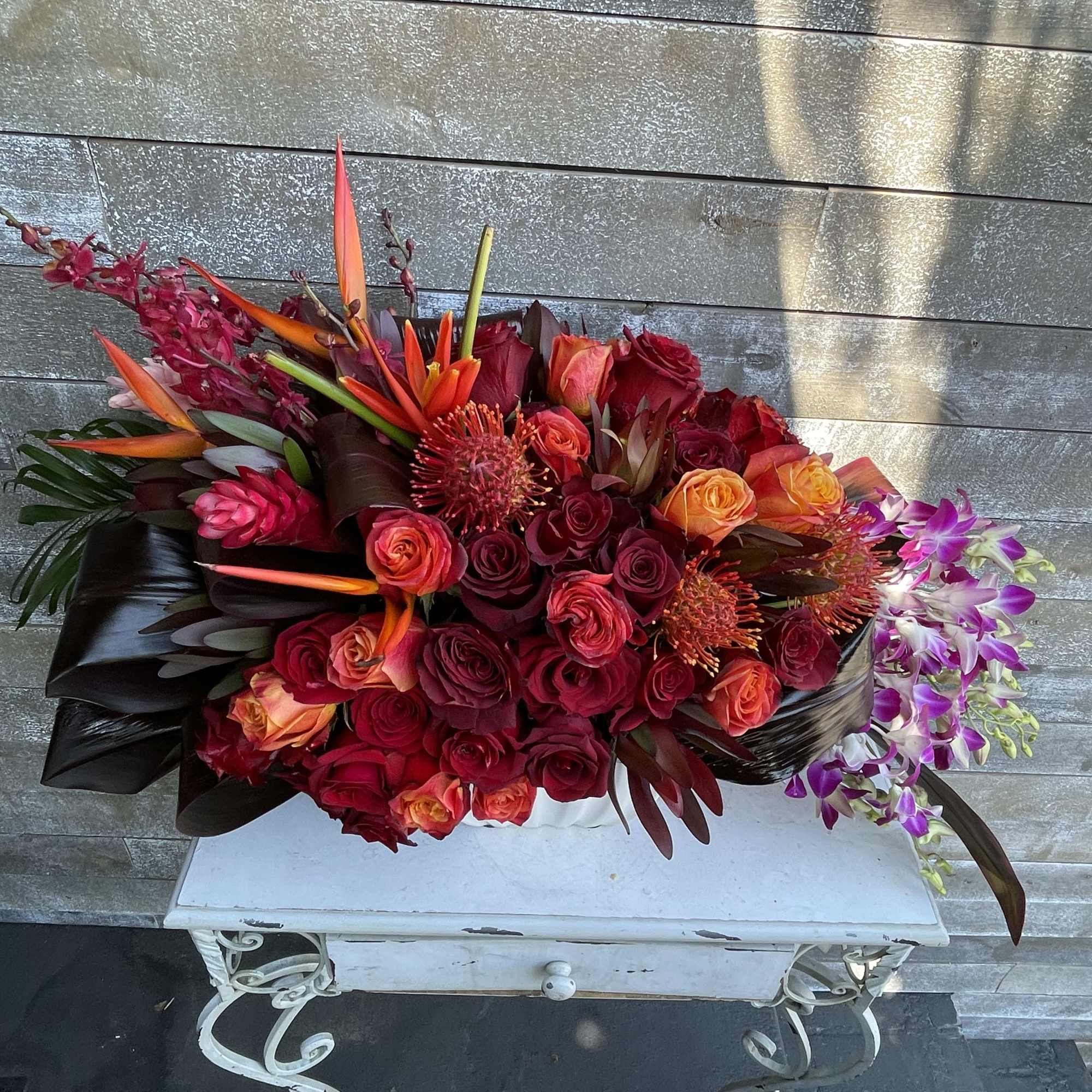 Large bouquet of red and orange roses with purple orchids in a black wrap