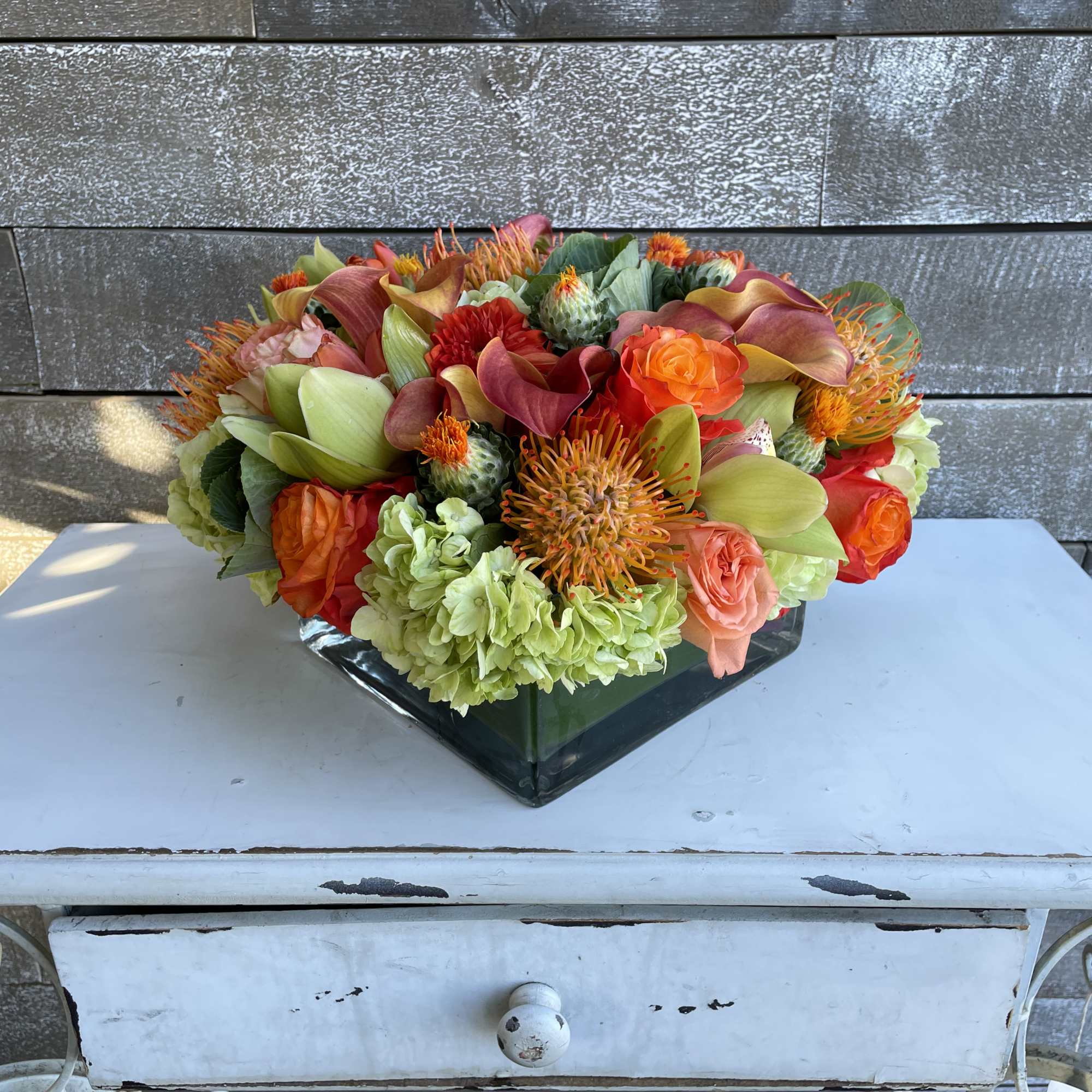 Mixed bouquet in a square glass vase with orange, red, and green blooms