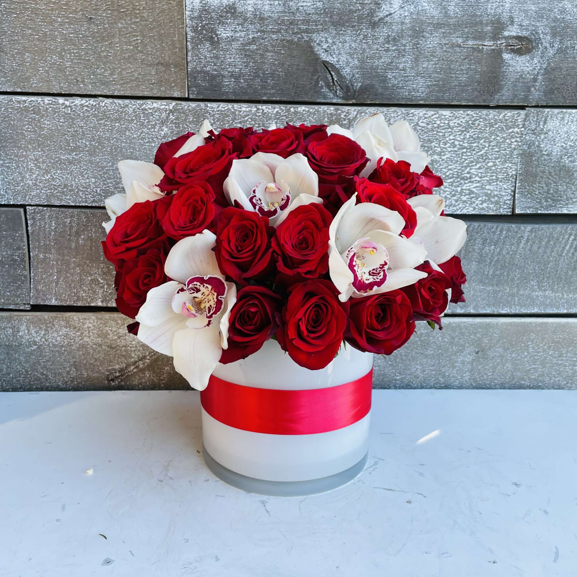 Red roses and white orchids in a white hat box with a red ribbon