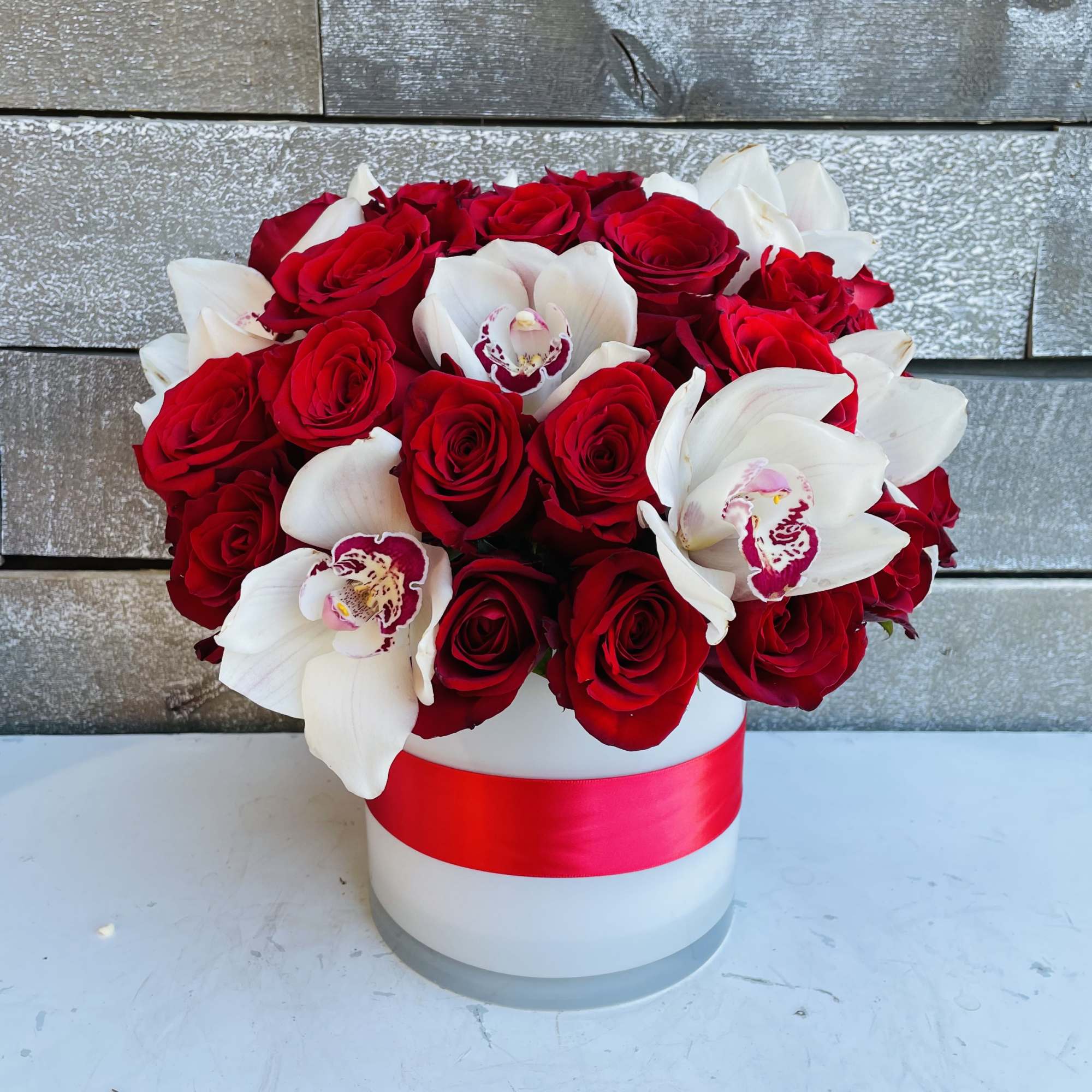 Red roses and white orchids arranged in a white hat box with a red ribbon