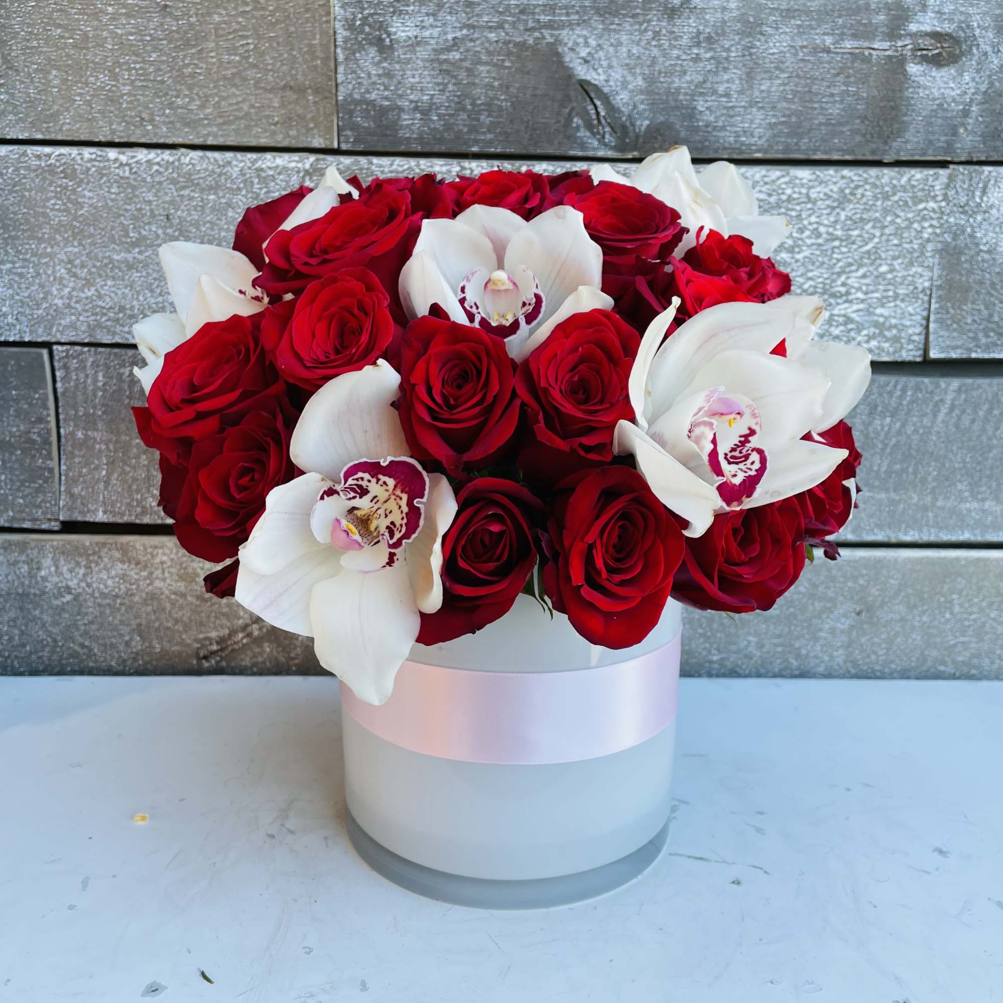 Red roses and white orchids arranged in a white round box