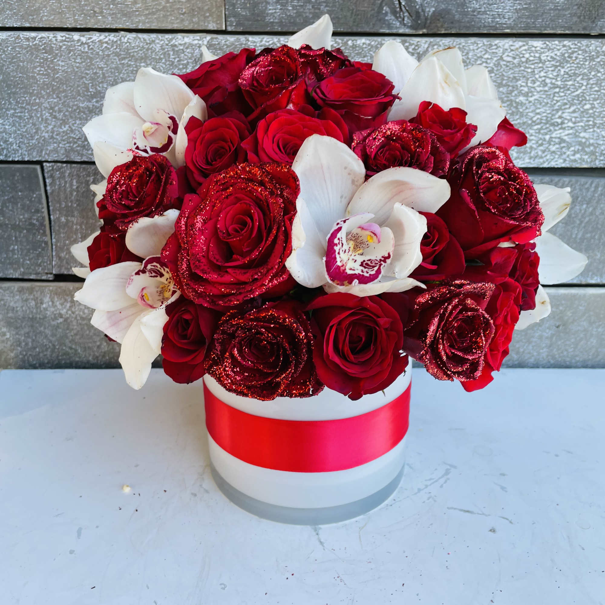 Red roses and white orchids in a white hatbox with a red ribbon