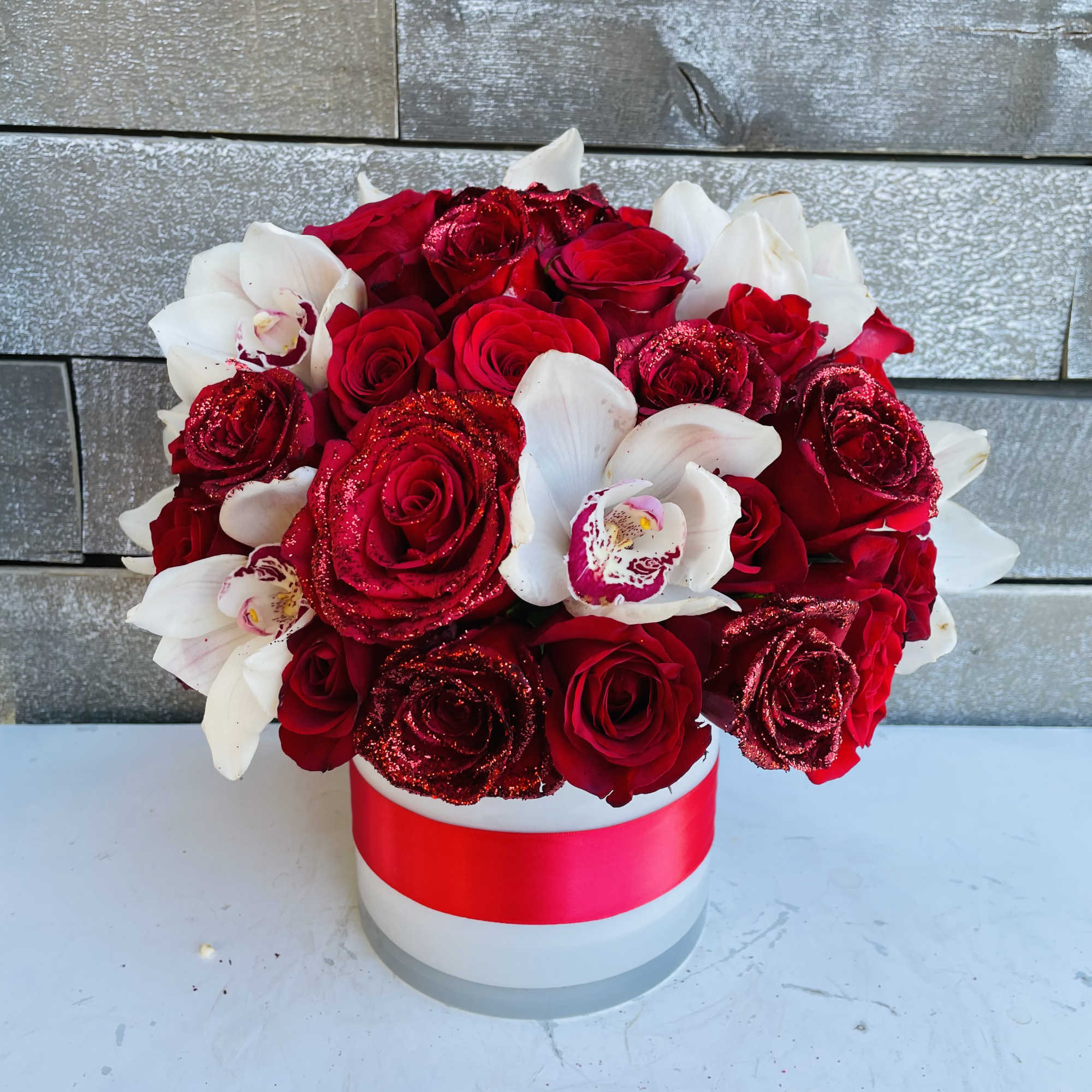 Red roses and white orchids in a white hat box with a pink ribbon