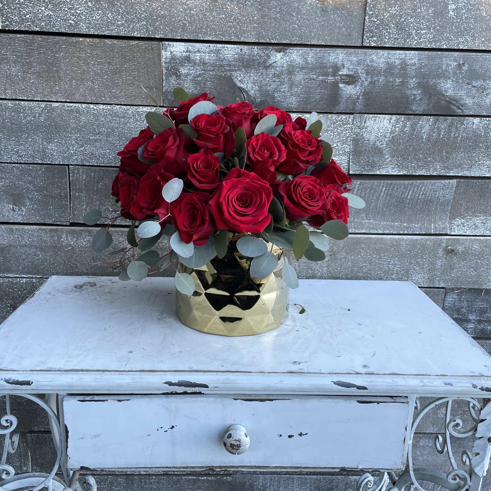 Red roses arranged in a gold vase with eucalyptus
