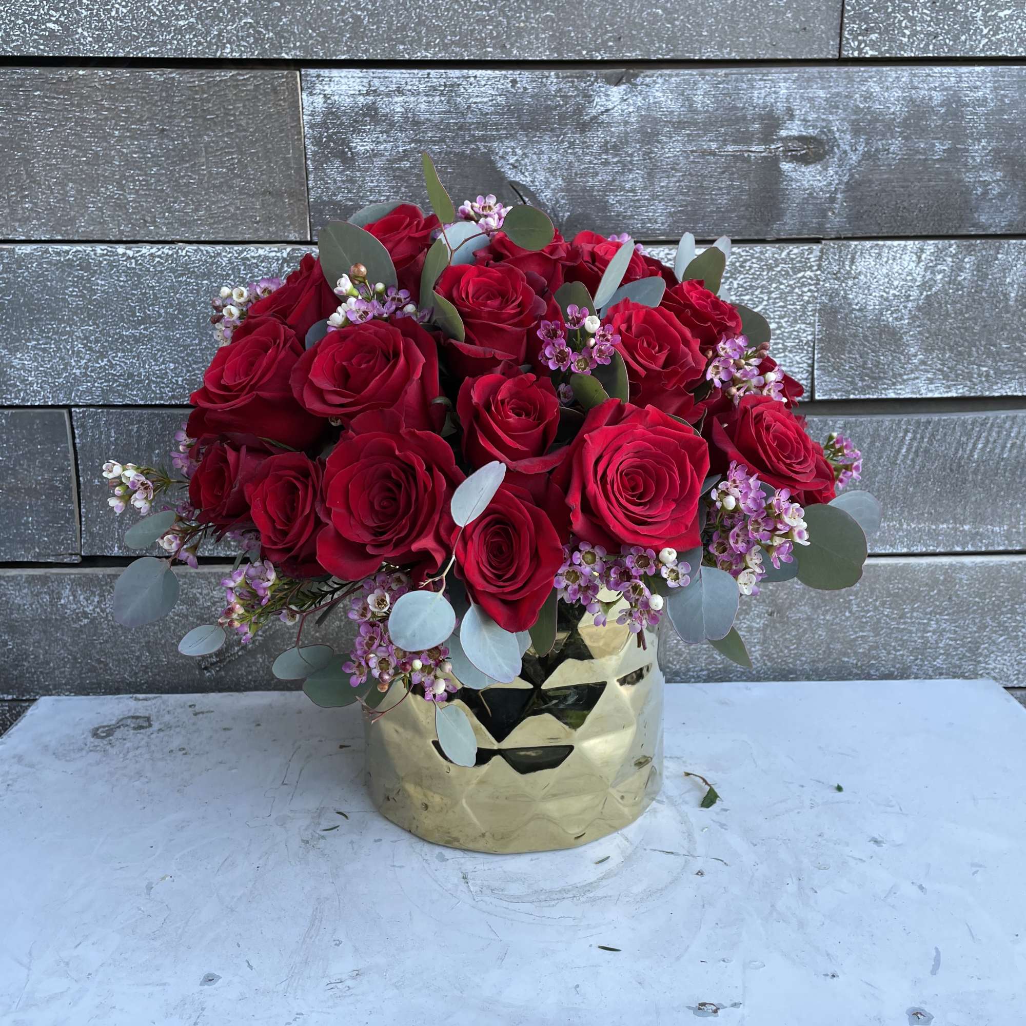 Red rose bouquet in a gold vase with small pink filler flowers