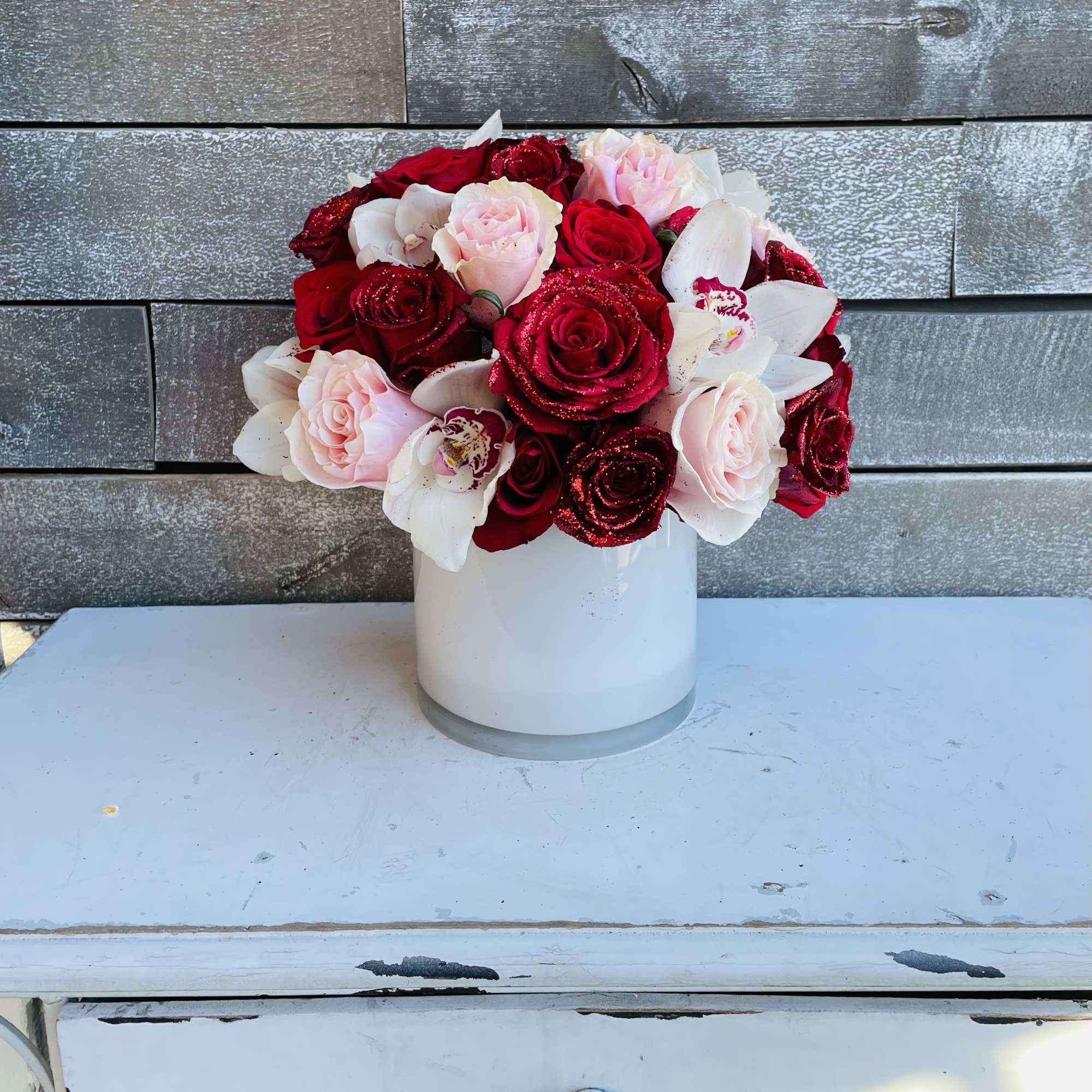 Red and pink roses with white orchids in a white vase
