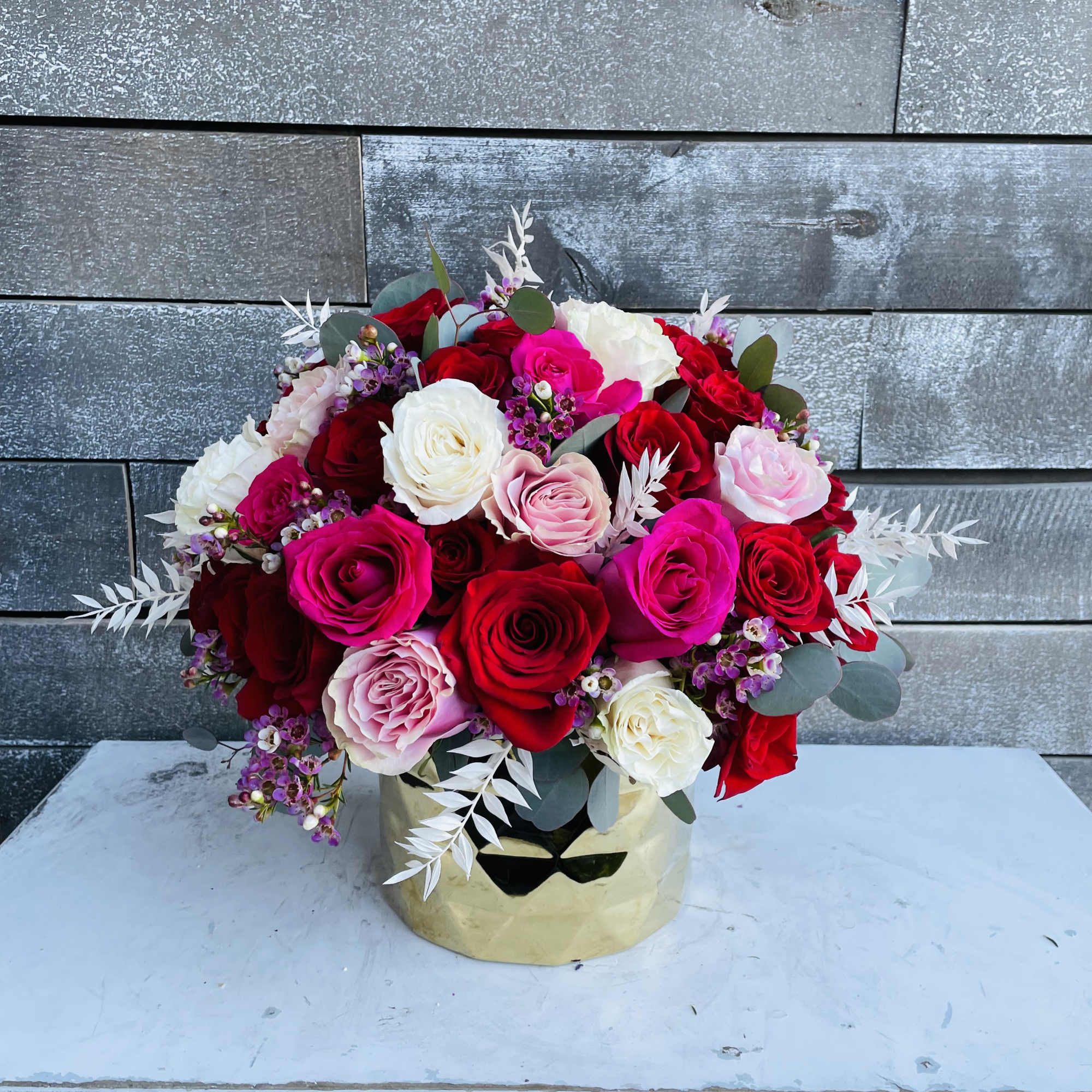 Round bouquet of red, pink, and white roses in a gold vase