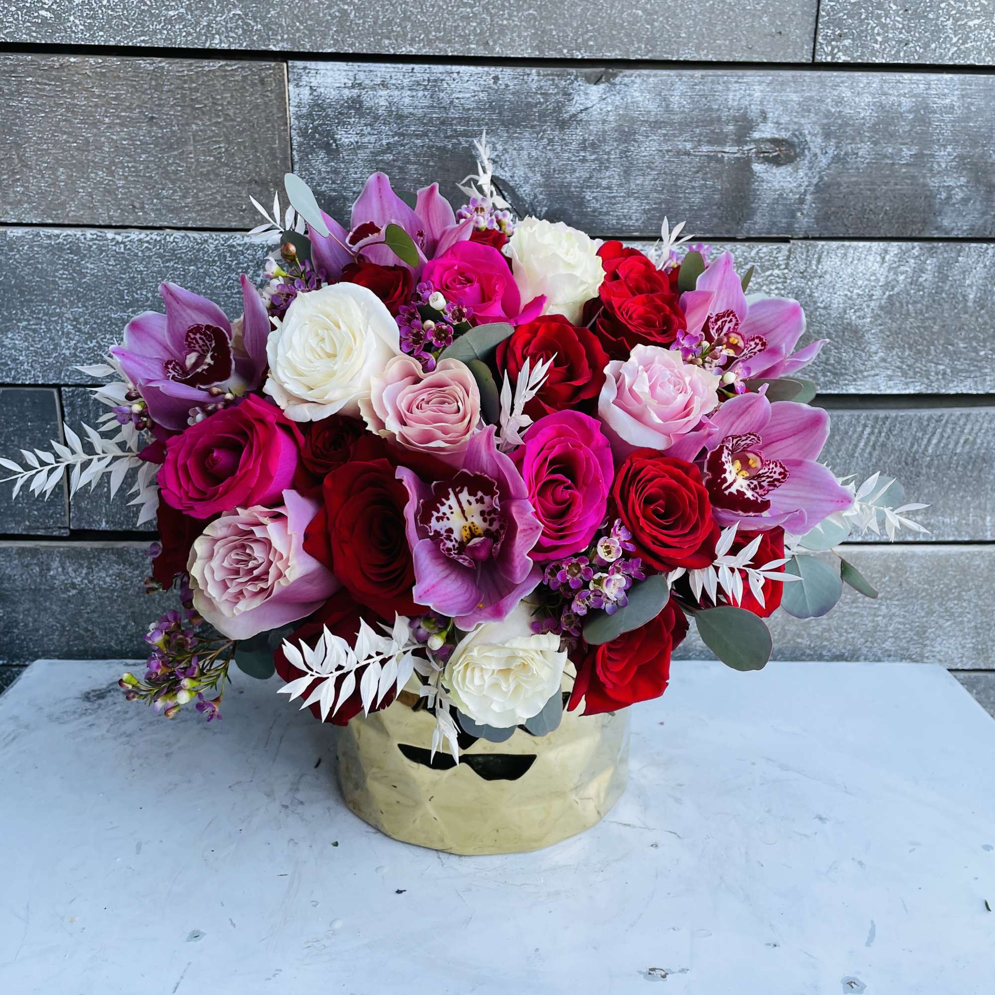 Bouquet of pink, red, and white roses with purple orchids in a gold box