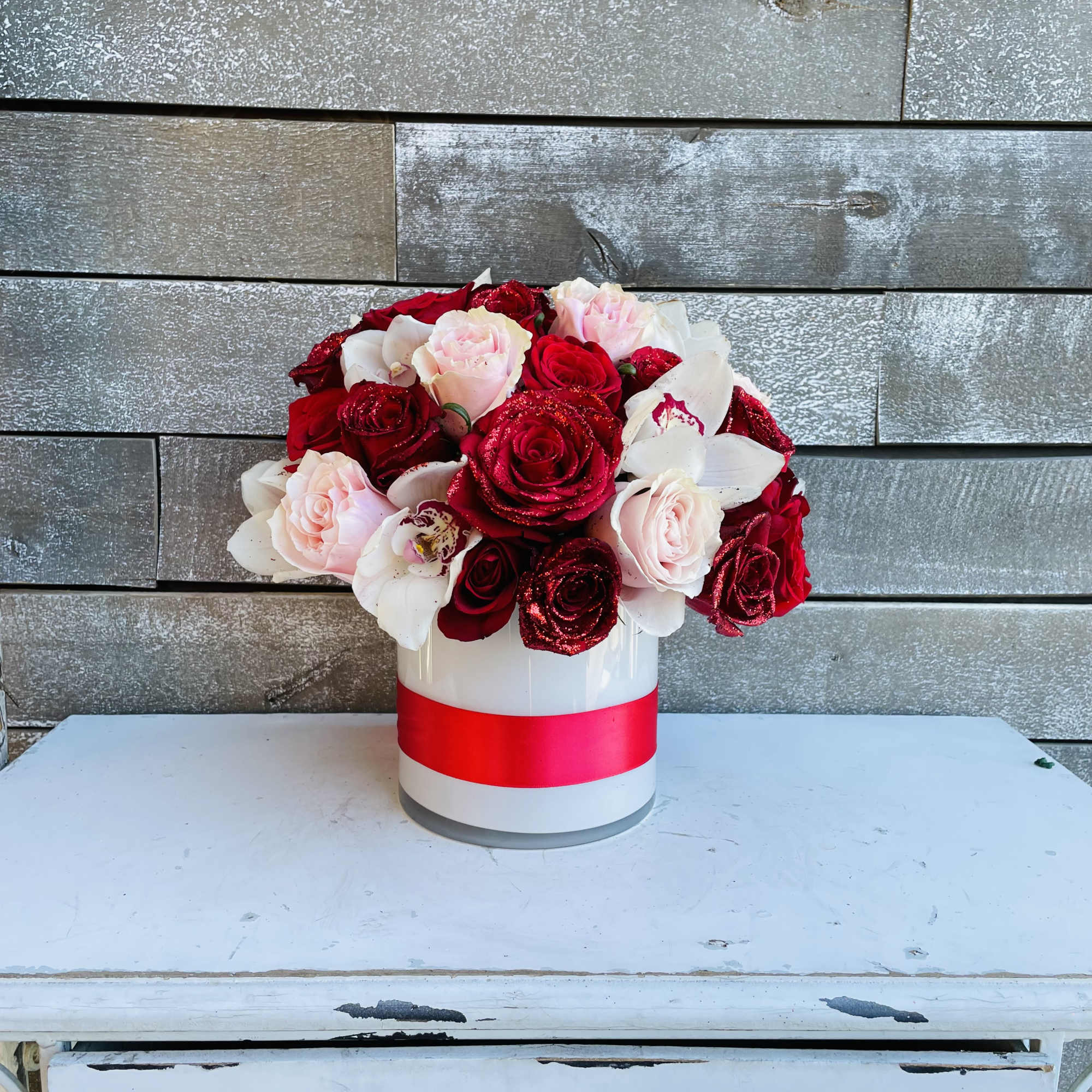 Red and blush roses arranged in a white hatbox with a pink ribbon