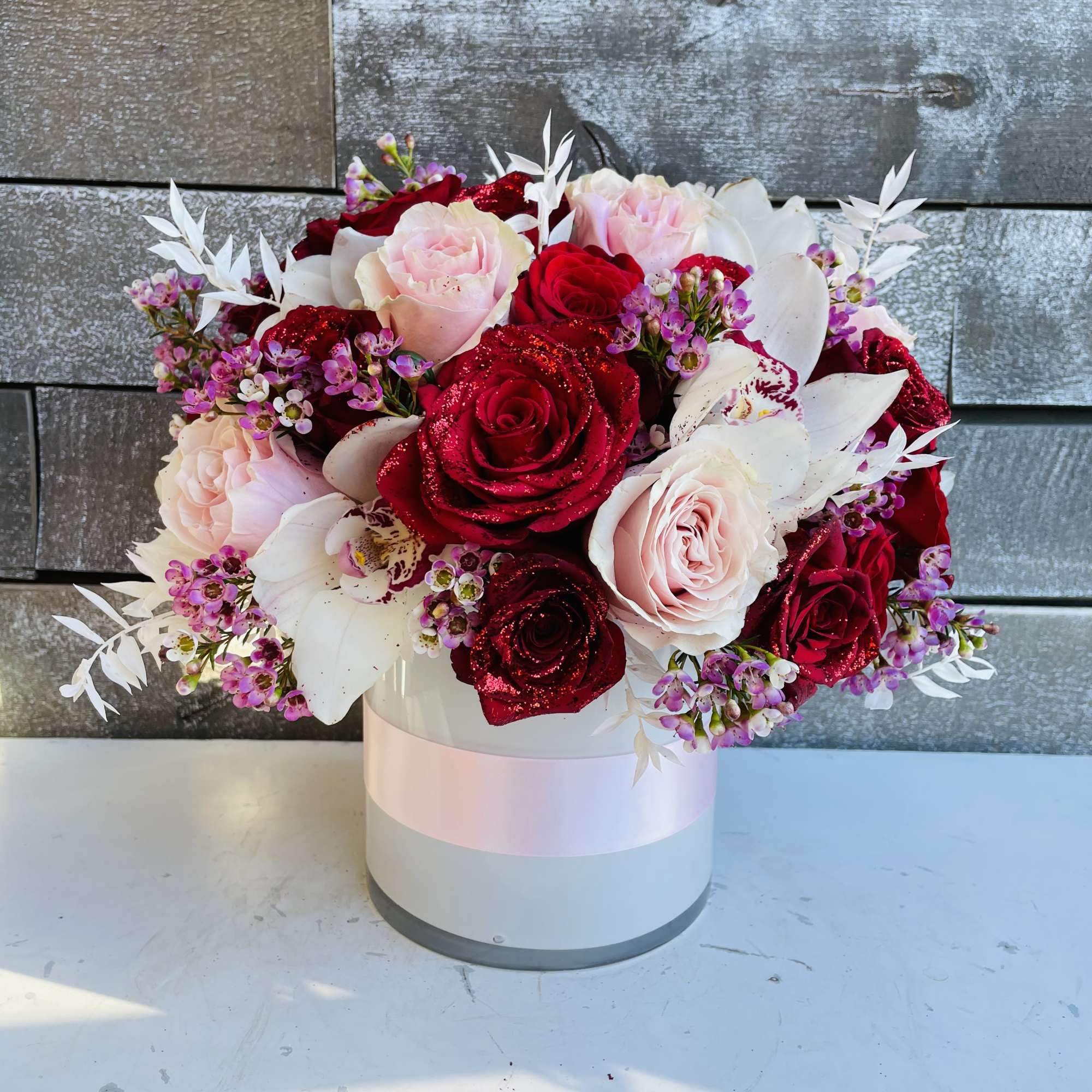 Bouquet of red and blush roses with white orchids in a round box