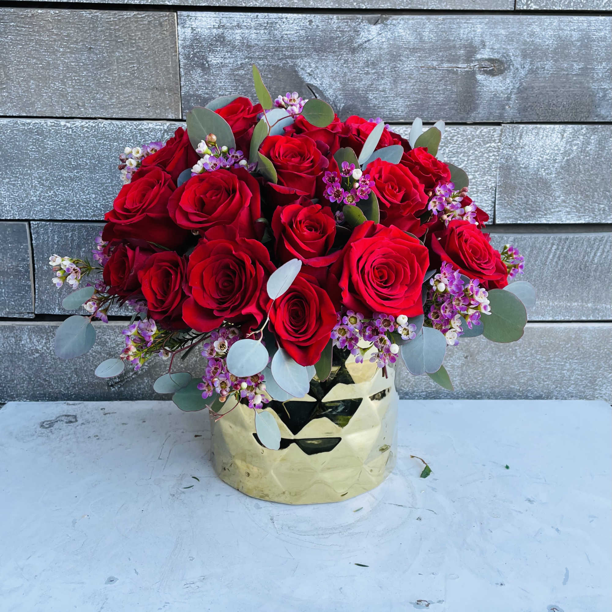Bouquet of red roses with small purple filler flowers in a gold vase