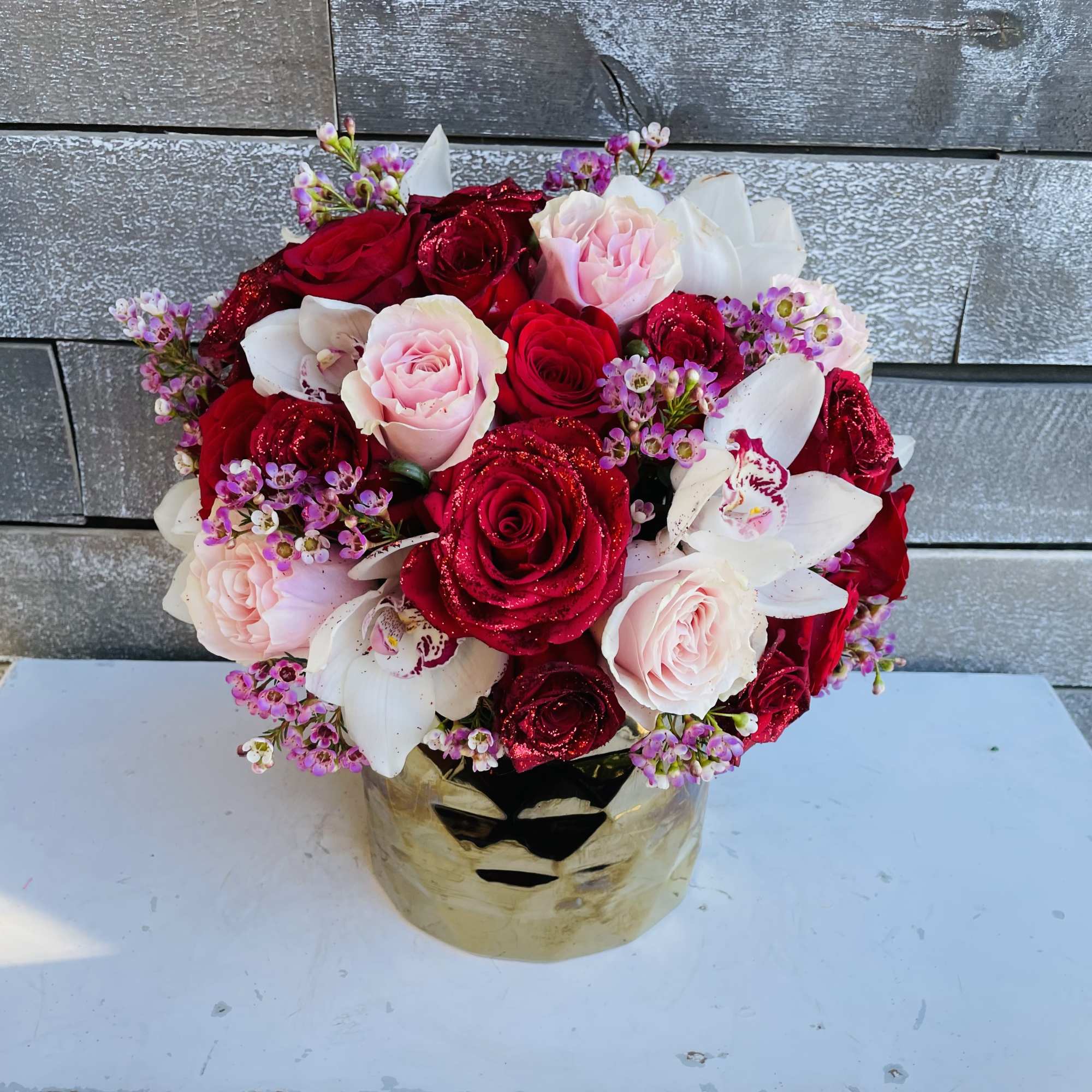 Bouquet of red and pink roses with white orchids in a gold vase