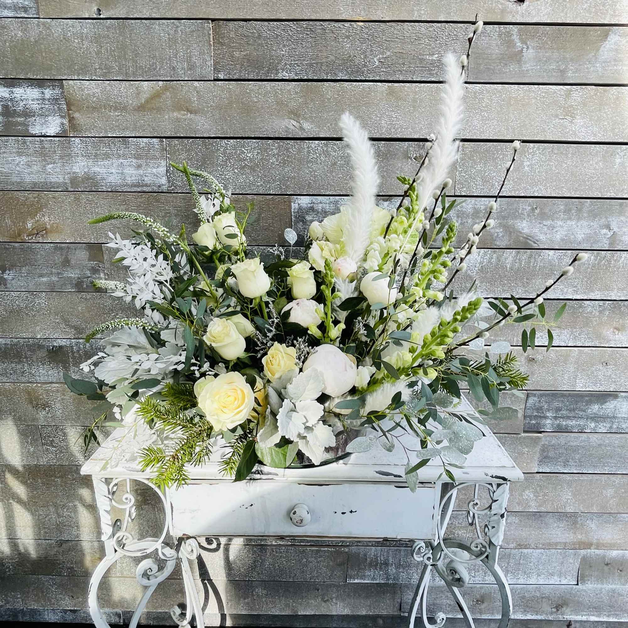 White rose arrangement in a white metal planter on a decorative table