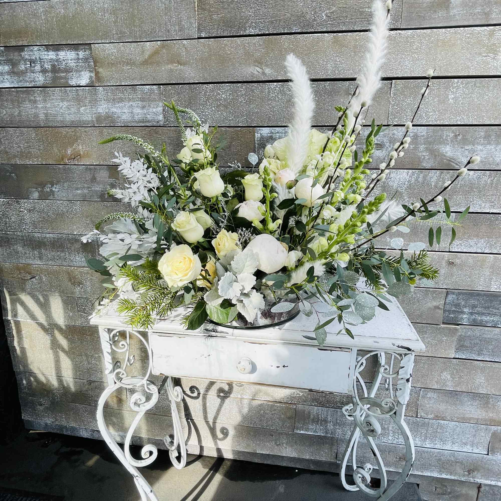 White floral arrangement with roses and tall feathery stems in a white table stand