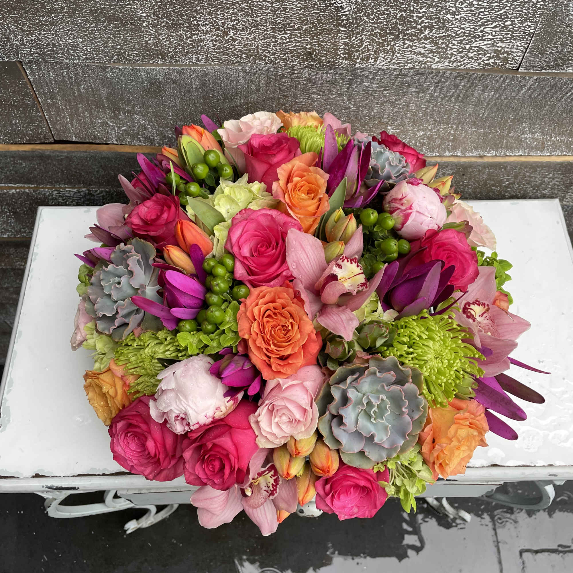 Round bouquet of pink, orange, and green flowers on a white surface