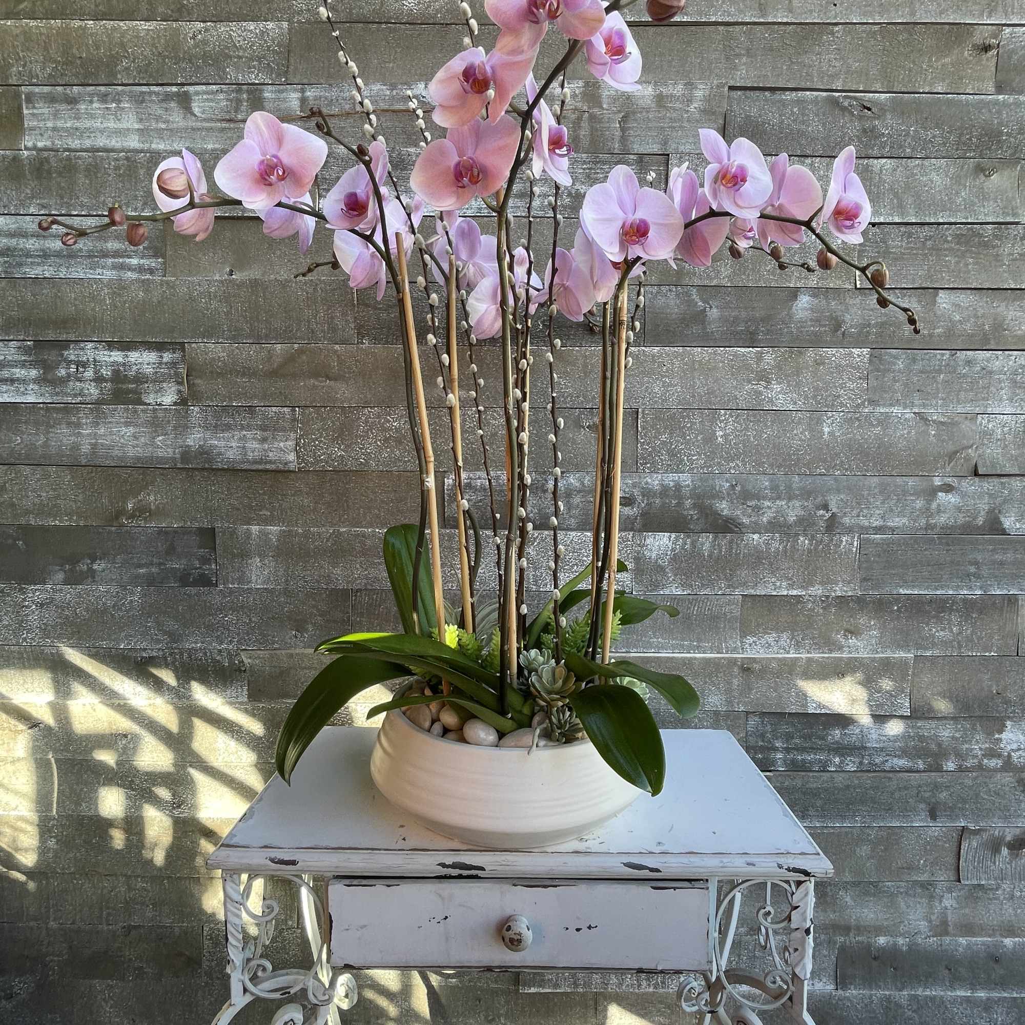 Pink orchid arrangement in a white bowl planter on a small table