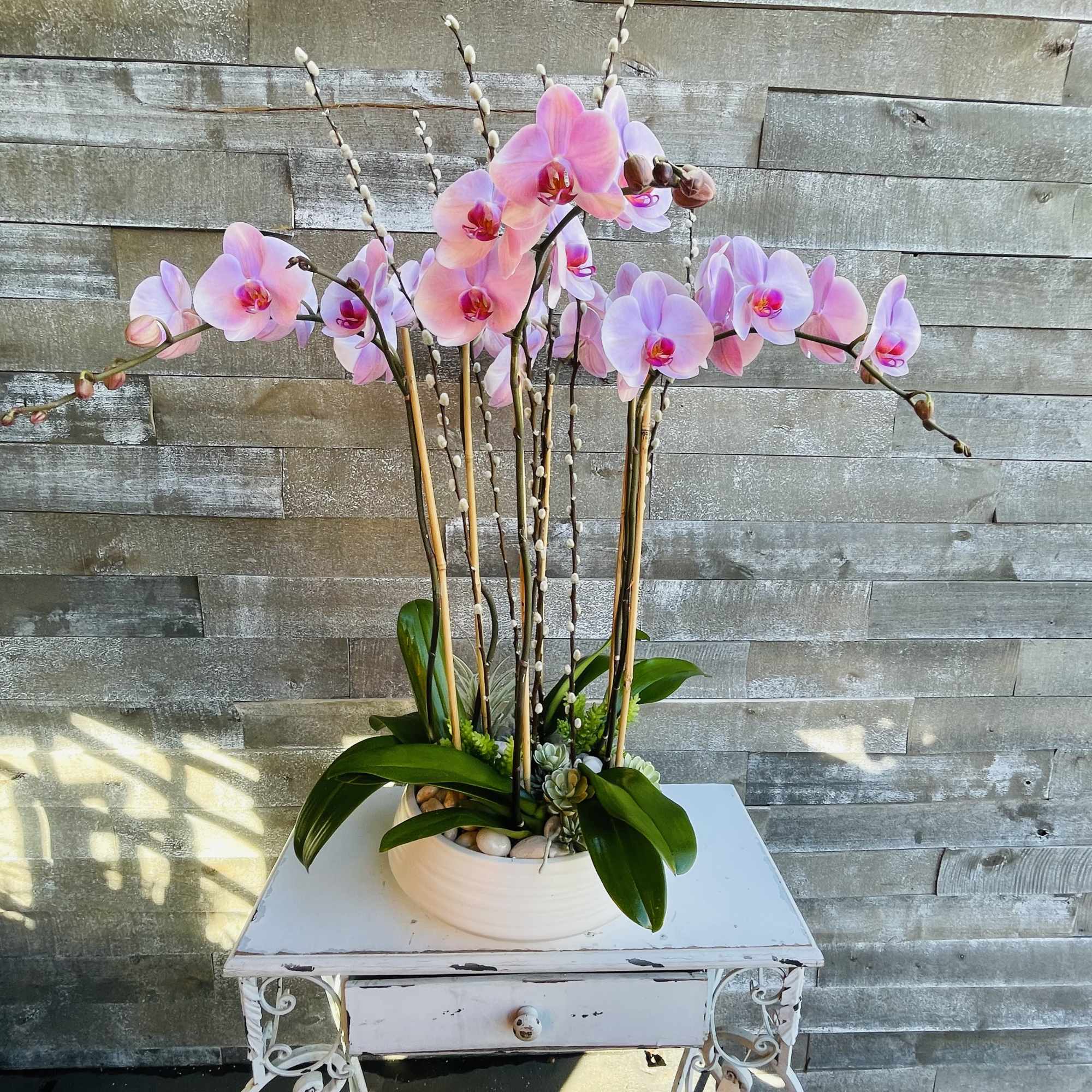 Pink orchid arrangement in a white bowl on a small table