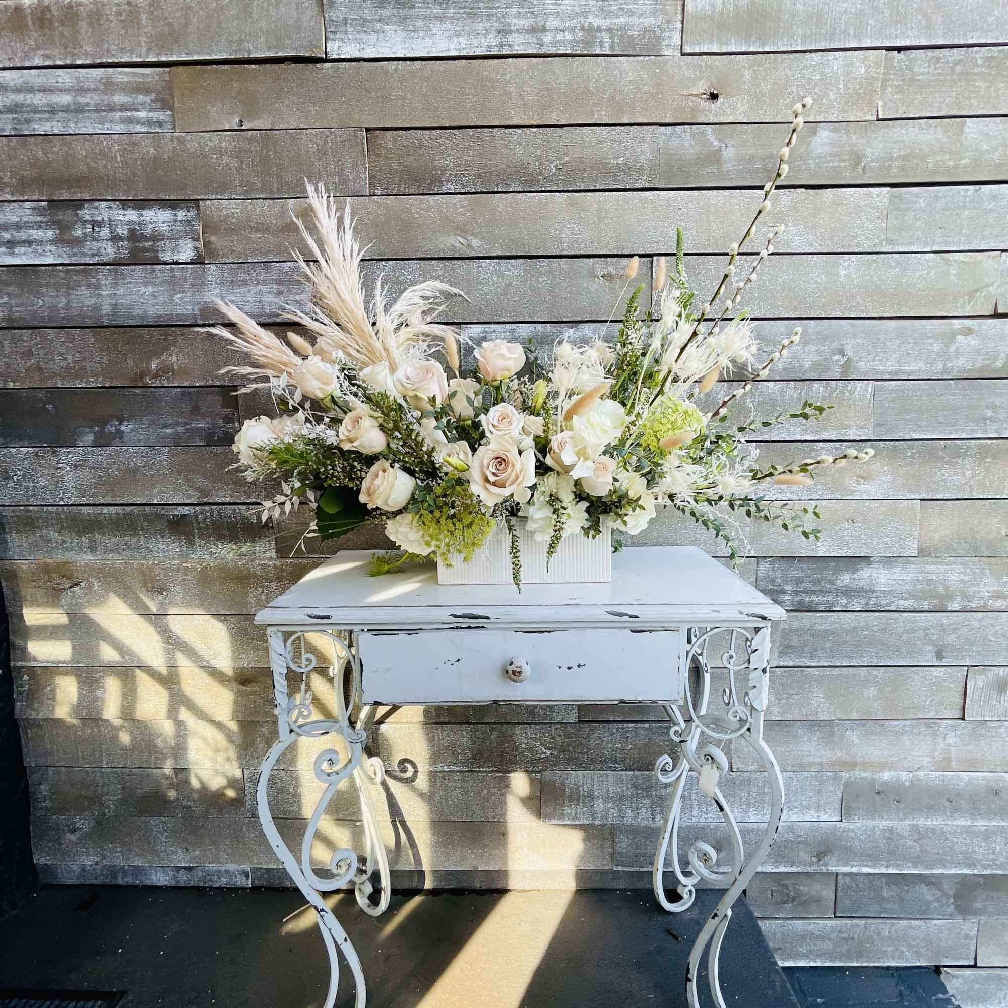 Cream and white floral arrangement in a white rectangular container on a small table