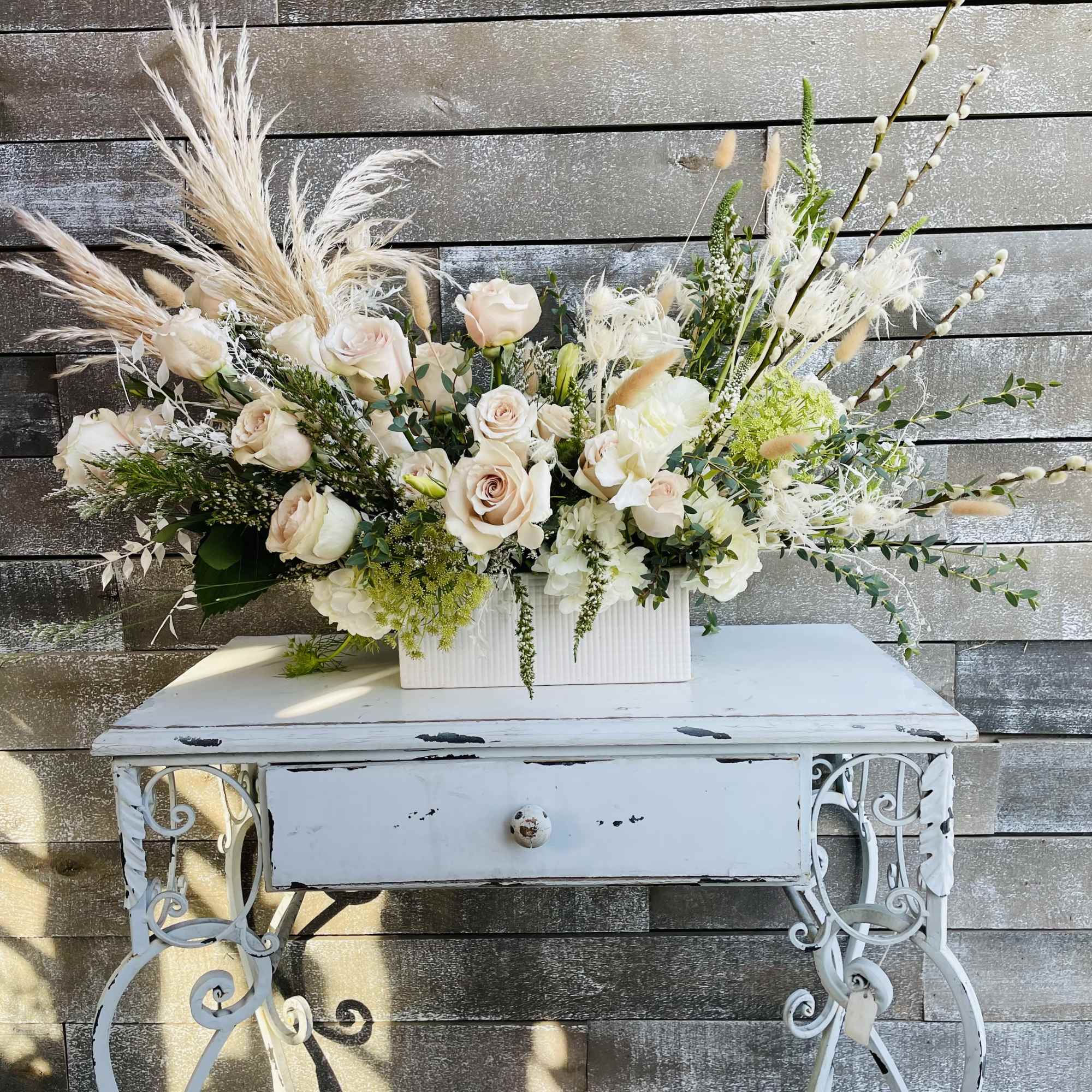 Large floral arrangement with pale roses and white blooms in a white rectangular vase