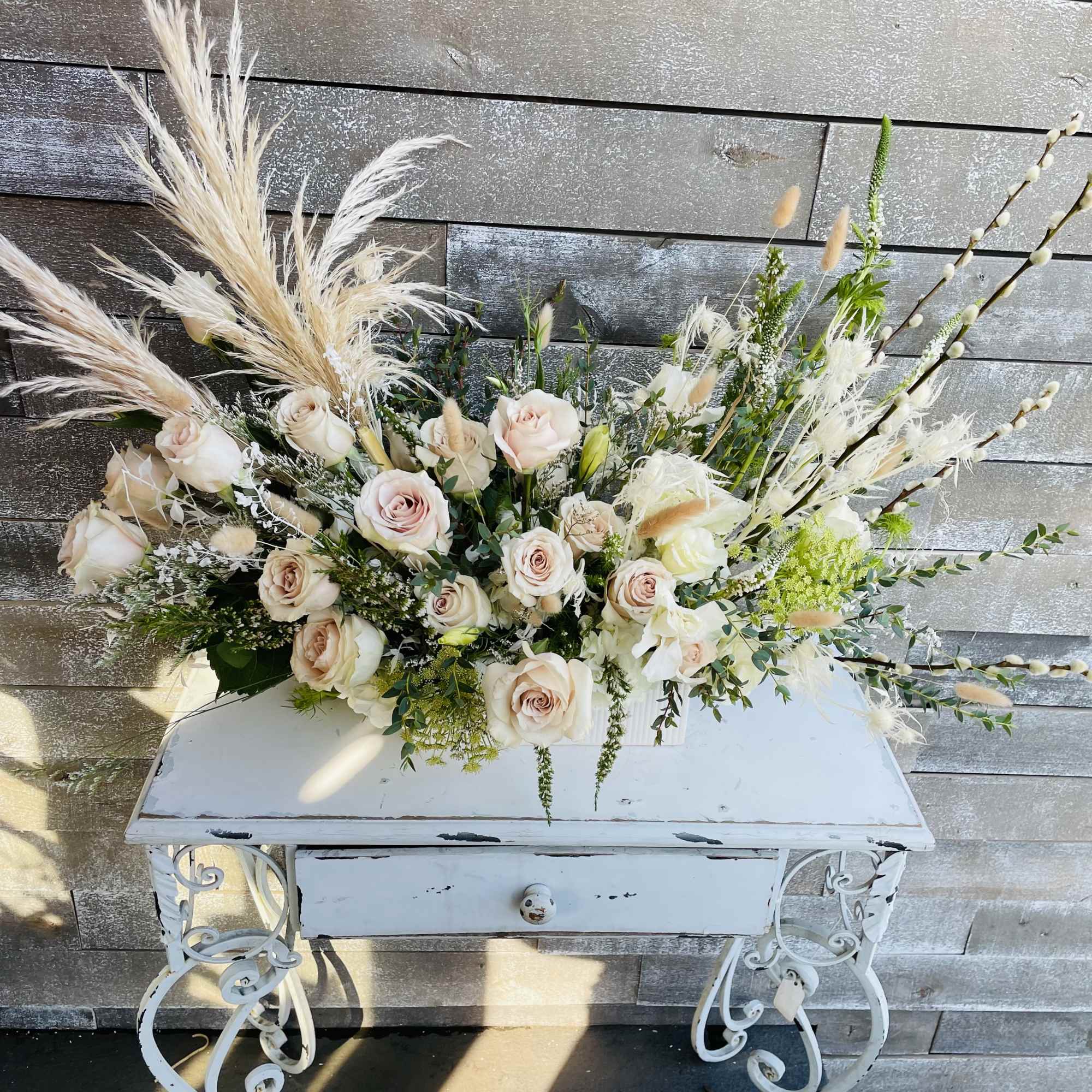 Large arrangement of pale roses and pampas grass in a white table