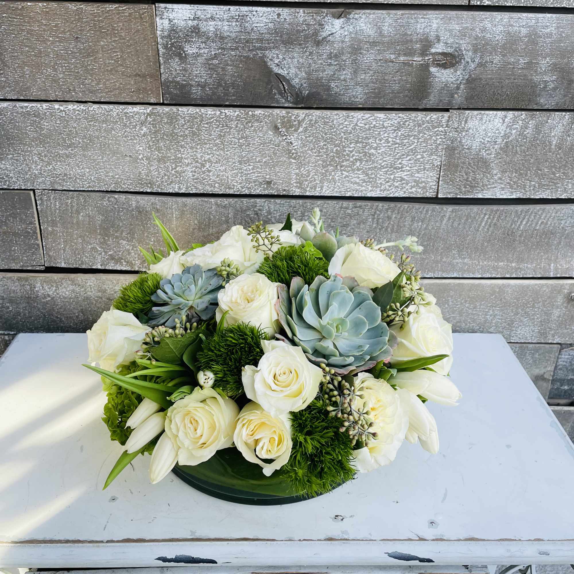 White roses and succulents arranged in a low round centerpiece