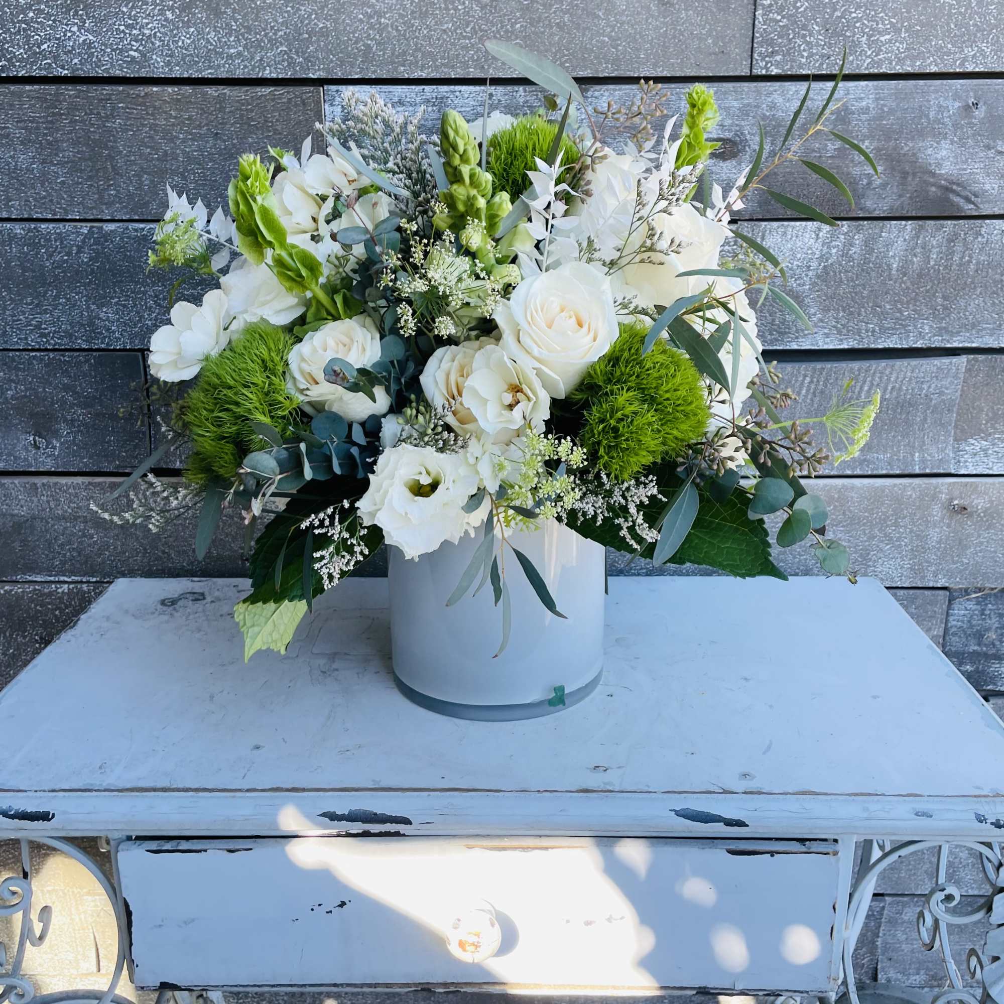 White floral arrangement in a white vase with green accents