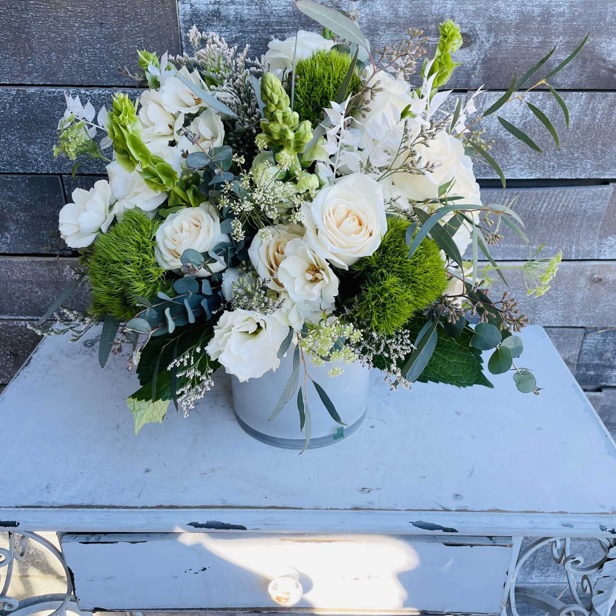 White floral arrangement in a round vase with bright green accents