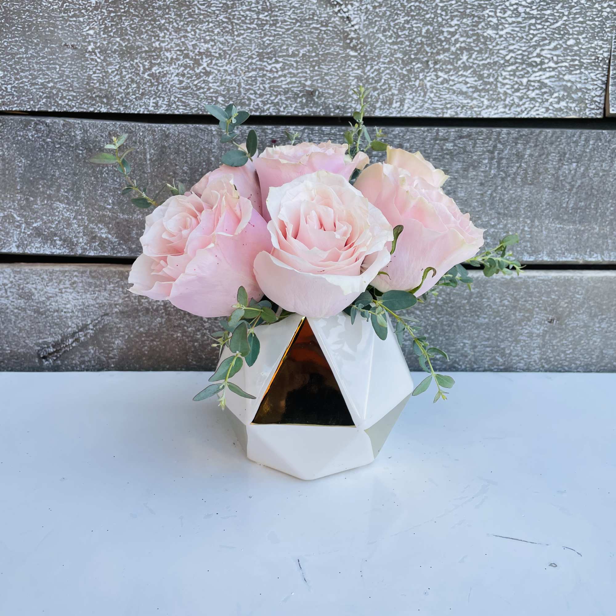 Pink roses arranged in a white geometric vase with trailing greenery