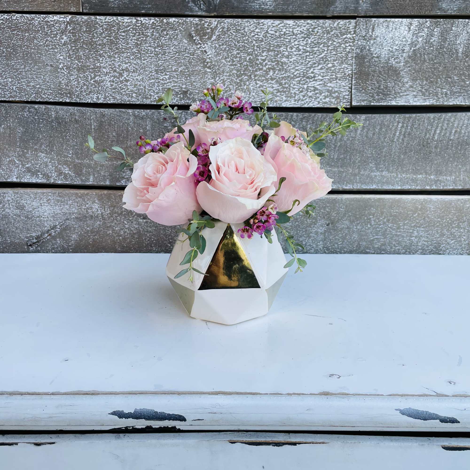 Pink roses in a geometric white vase with small purple flowers