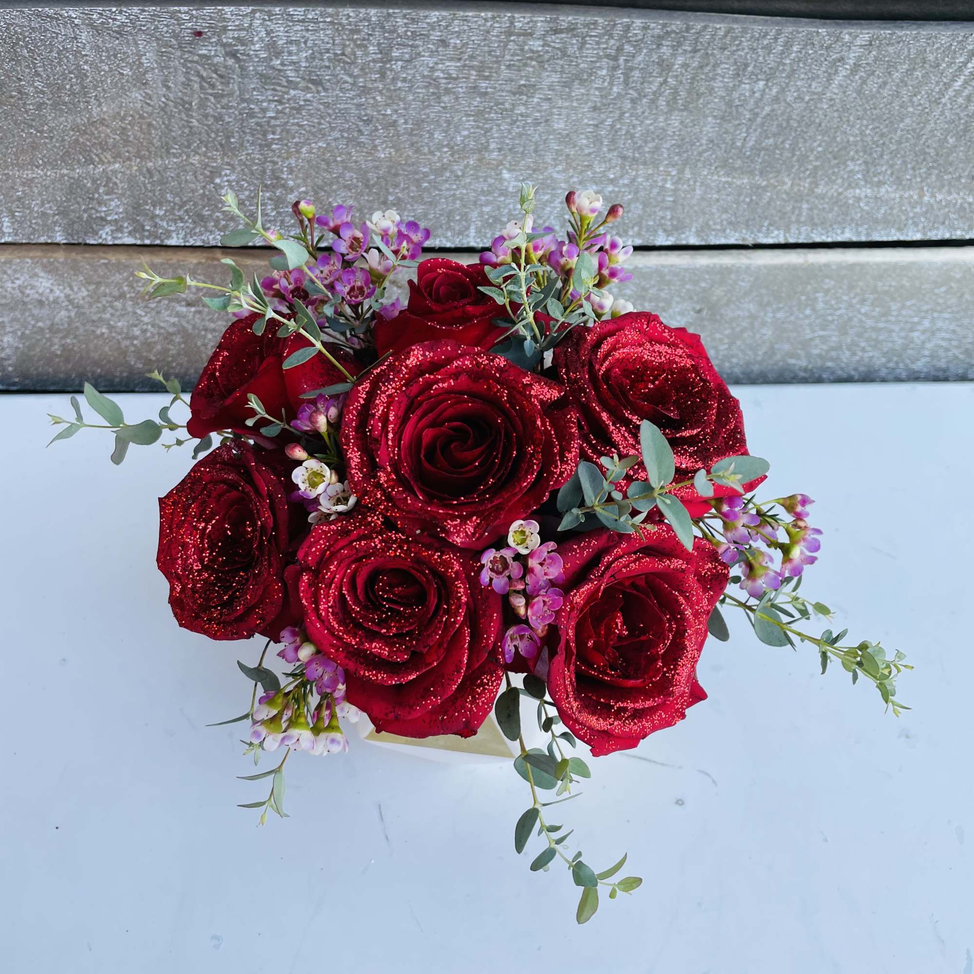 Red glitter roses with small pink filler flowers and eucalyptus in a low arrangement