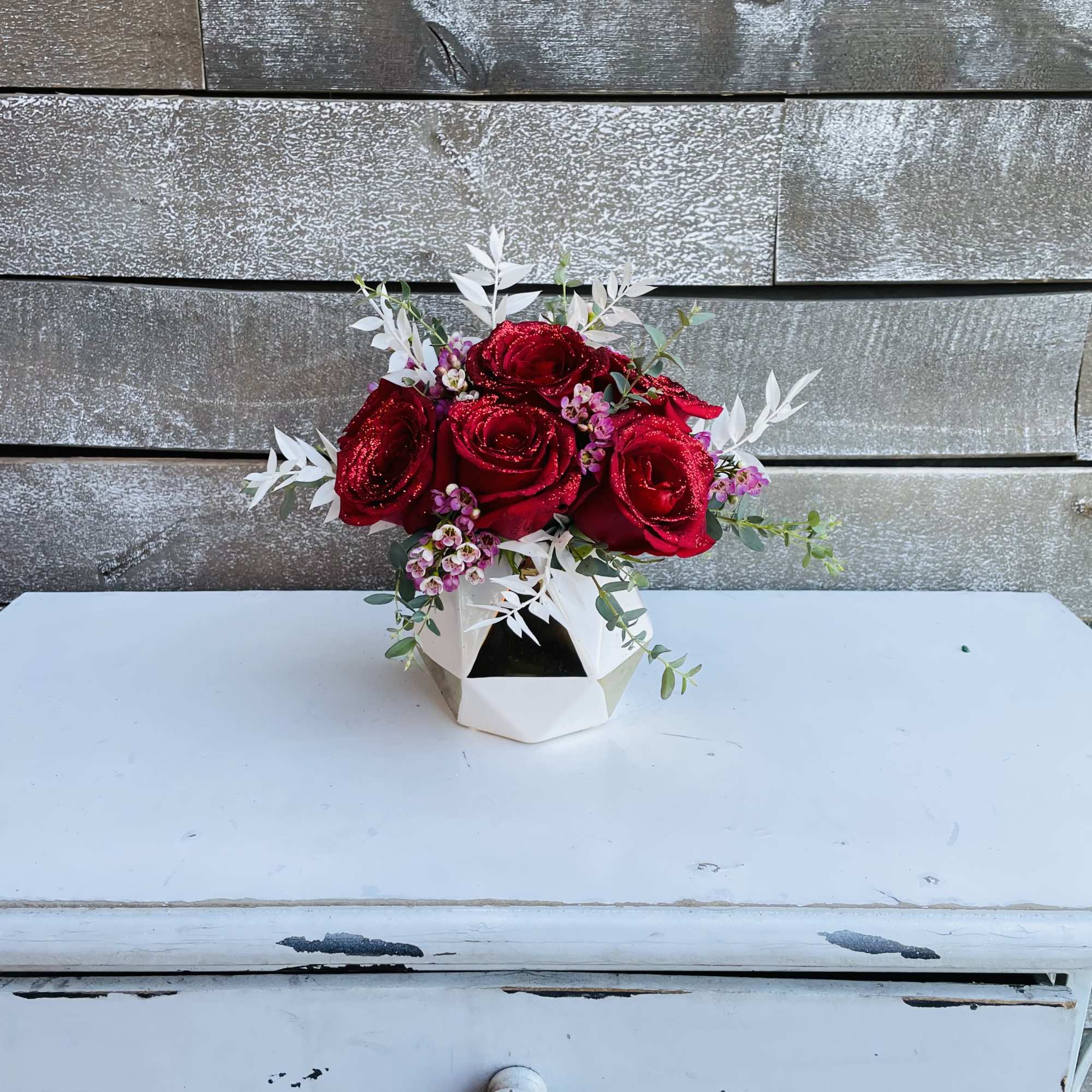 Red roses in a white geometric vase with small pink flowers