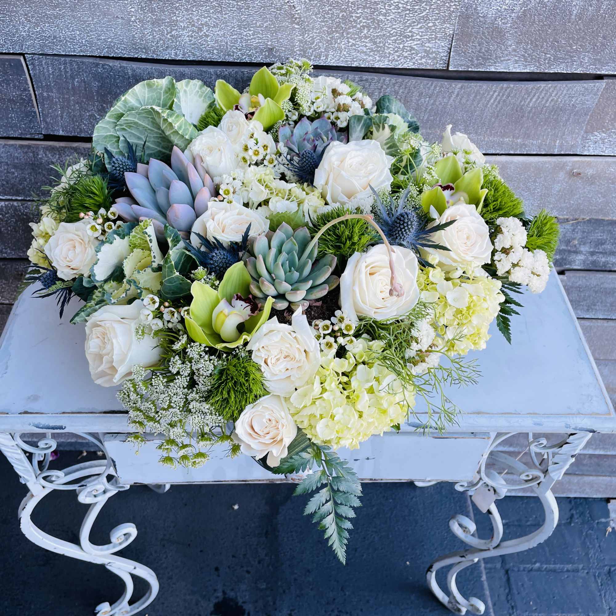 Low floral arrangement with white roses, succulents, and green orchids