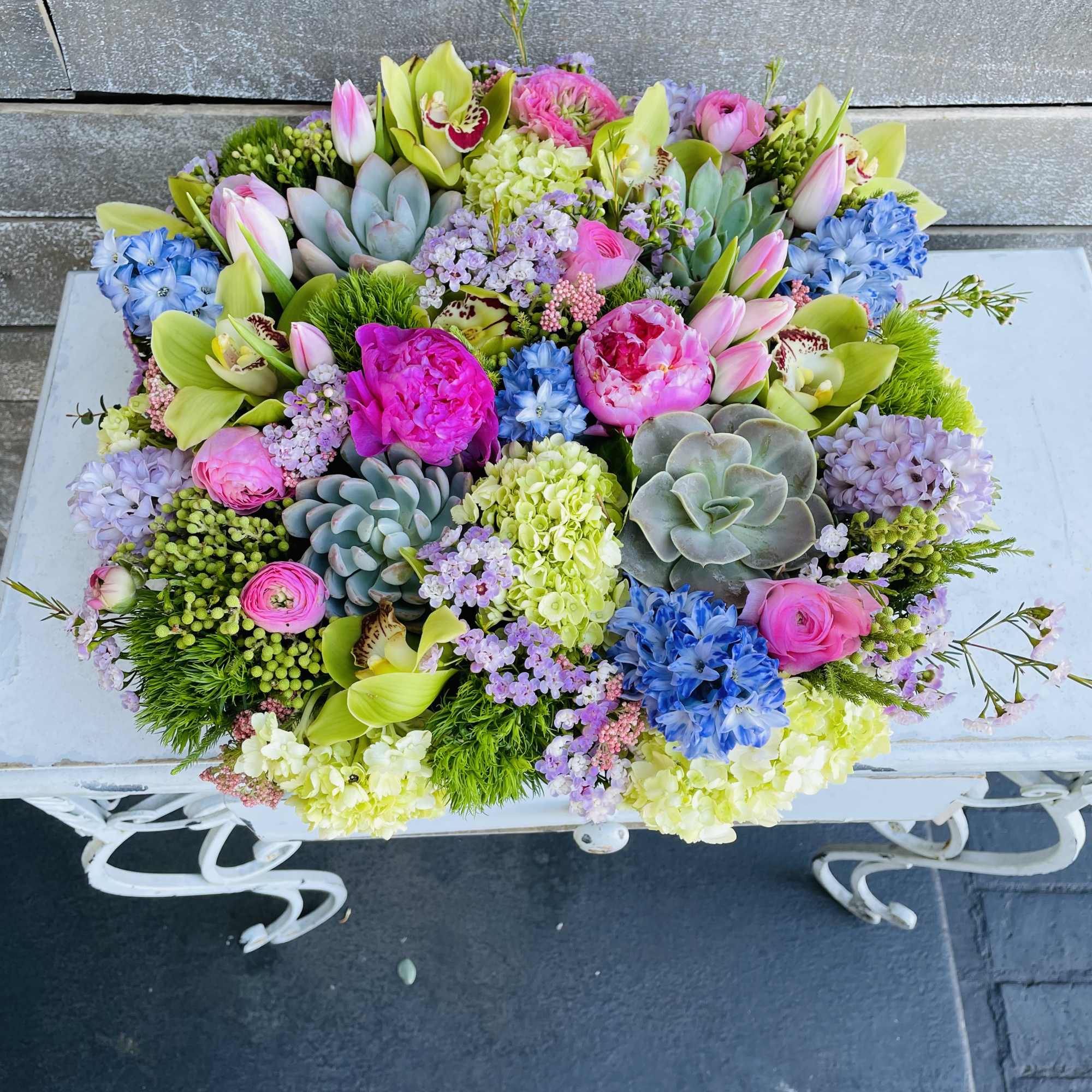 Colorful mixed floral arrangement with succulents and orchids in a white container