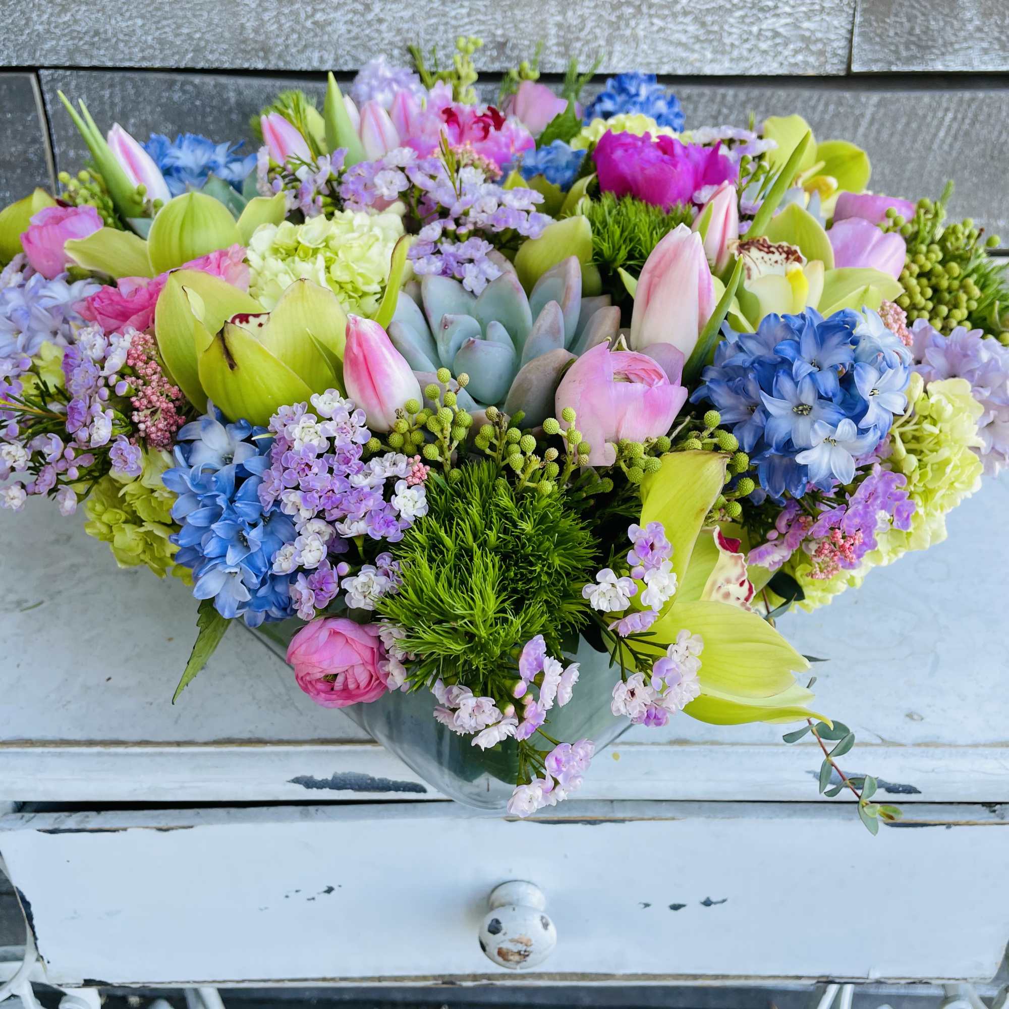 Colorful mixed bouquet in a glass vase with pink, blue, and green blooms