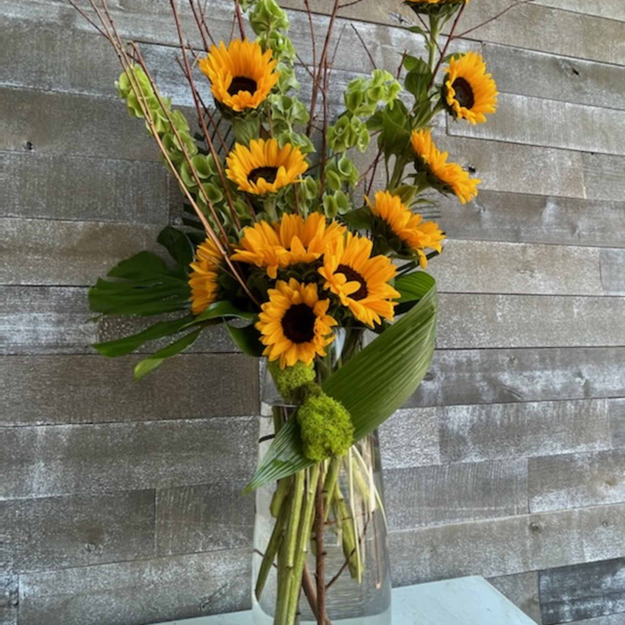 Sunflower arrangement in a clear glass vase with tall branches and green accents
