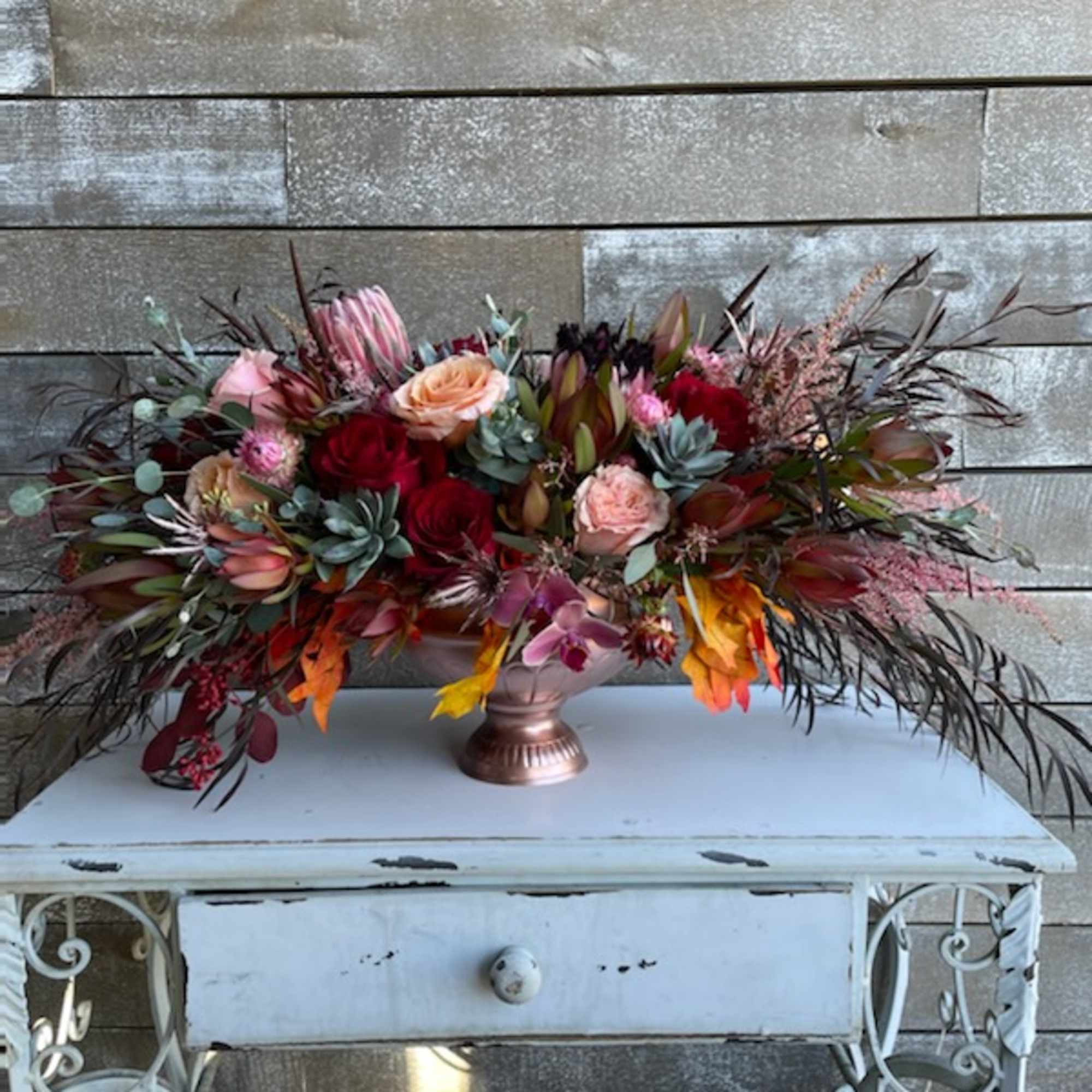 Large mixed floral arrangement in a copper vase with red, pink, and orange blooms