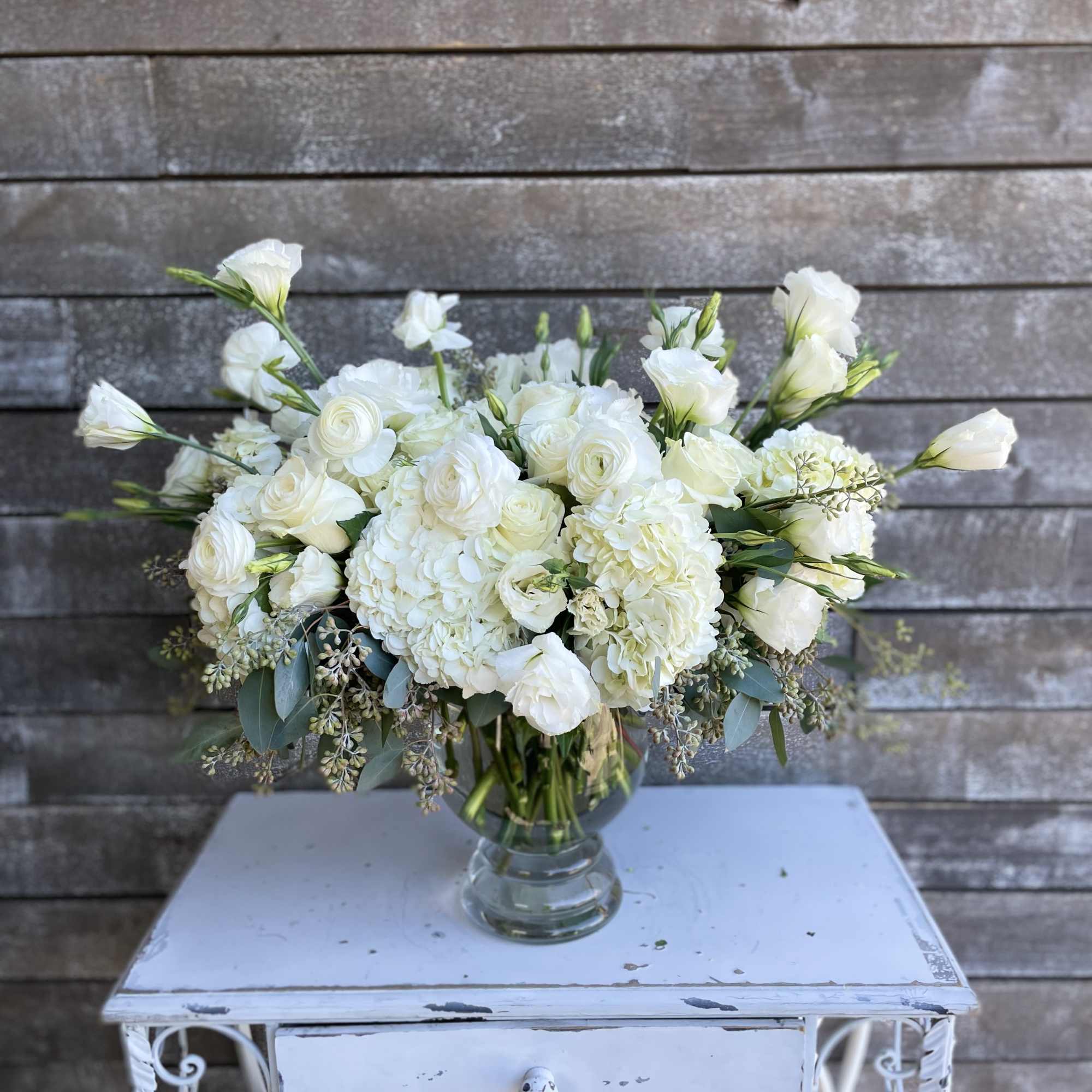 White floral arrangement in a clear glass vase on a small table, photo 2 of 3